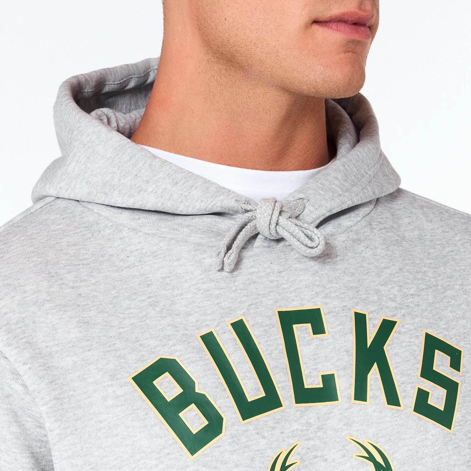 New Era Milwaukee Bucks NBA Grey Pullover Hoodie, front view showing a light grey fabric with a large green BUCKS wordmark outlined in yellow across the chest, hood with drawstrings and visible upper portion of a person's torso wearing the hoodie.