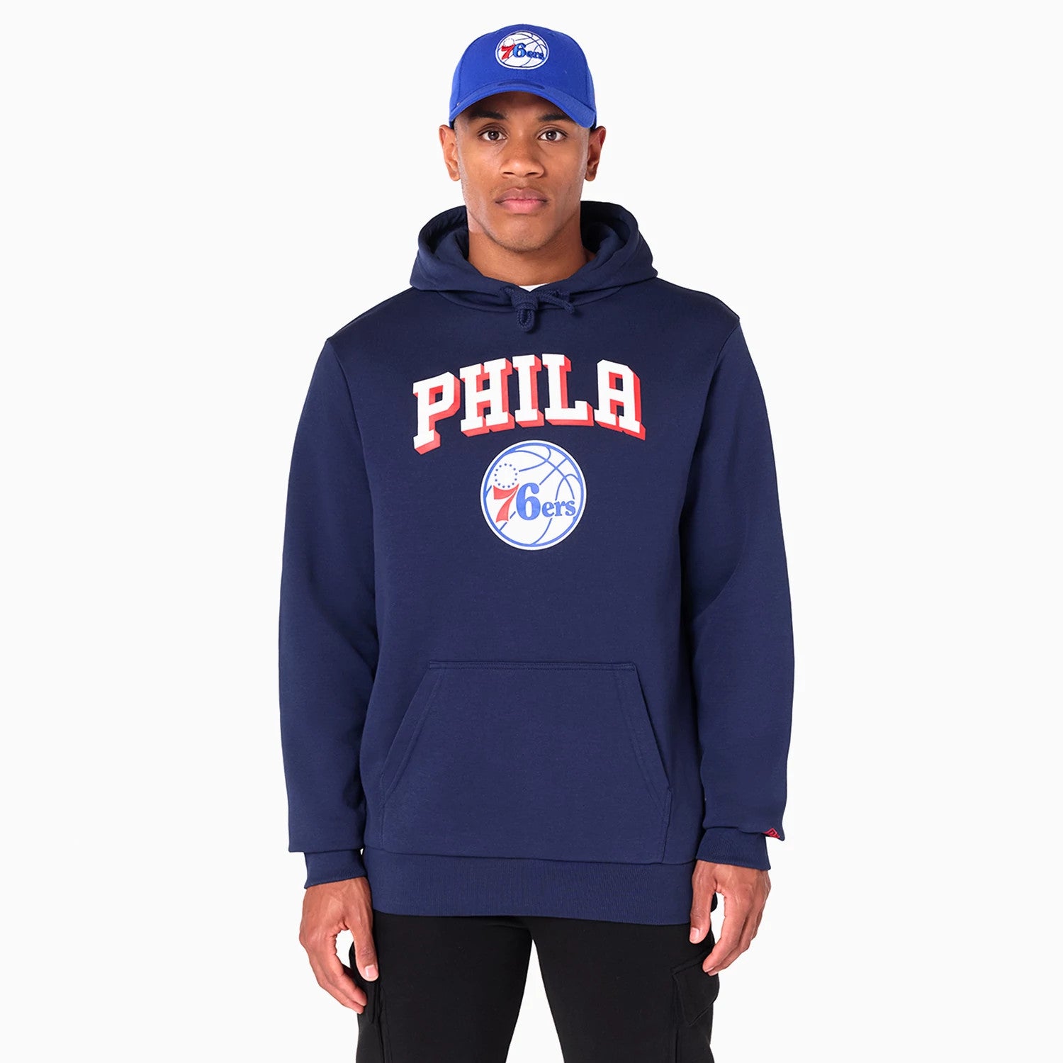 New Era Philadelphia 76ers NBA Navy Pullover Hoodie, front view showing the navy hoodie with PHILA lettering in red above the 76ers basketball logo on the chest and worn by a model wearing a blue cap with the same logo on the crown.