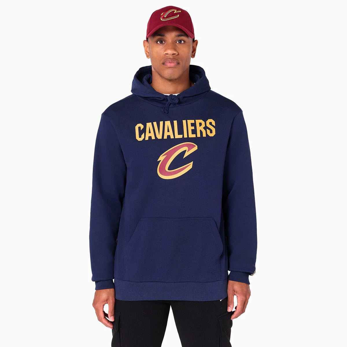New Era Cleveland Cavaliers NBA Navy Pullover Hoodie, front view showing the navy pullover with Cavaliers in gold lettering above a large team logo, model wearing a matching red cap with a raised team logo at the centre.