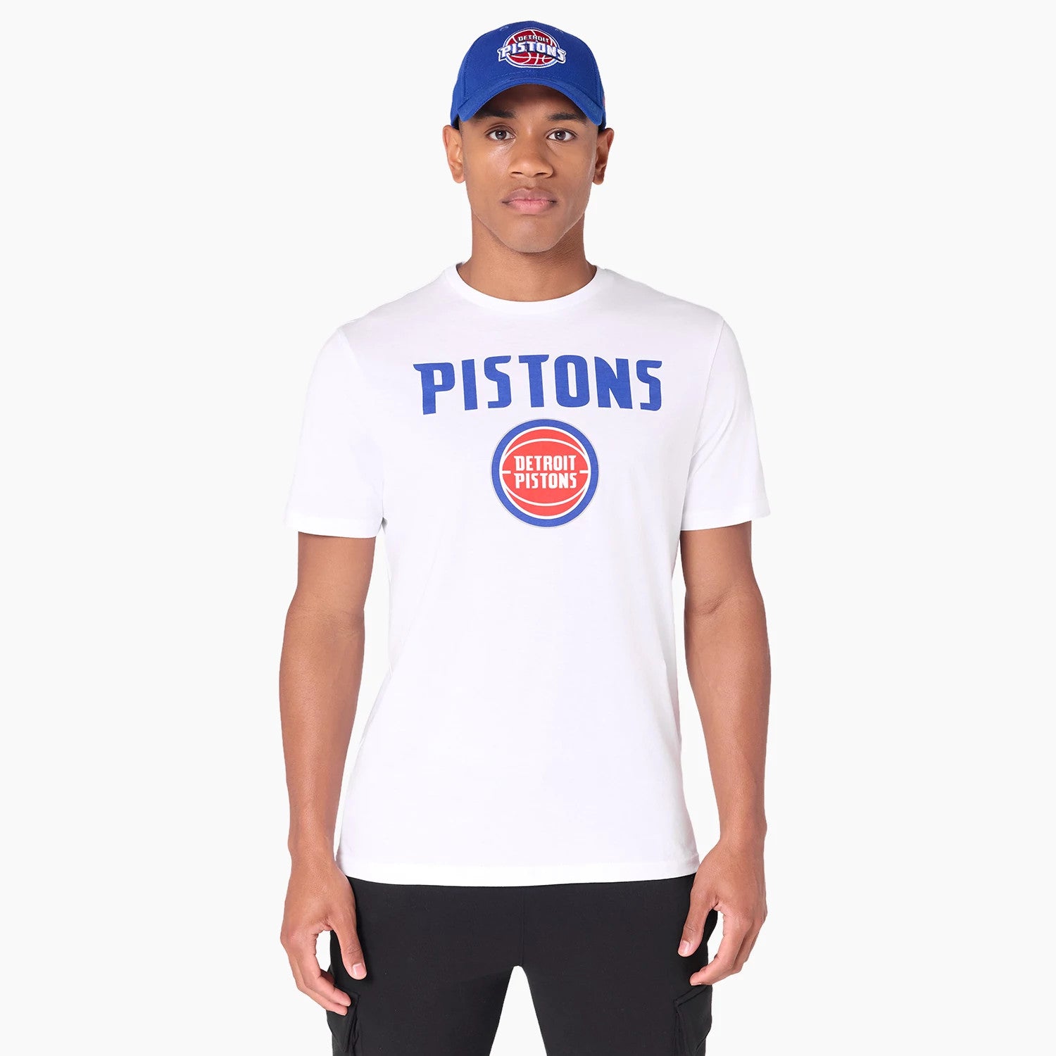 New Era Detroit Pistons NBA White T-Shirt, on-model view featuring the front design with bold blue PISTONS text and the red circular Detroit Pistons logo on a white background, paired with a blue cap displaying the embroidered team logo.