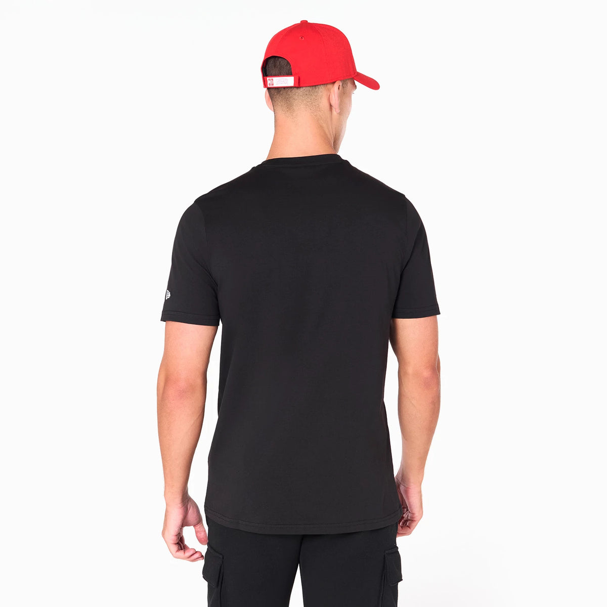 New Era Atlanta Hawks NBA Black T-Shirt, rear view showing the plain black fabric with short sleeves, a small debossed New Era logo on the left sleeve, and a man wearing a red cap facing away.