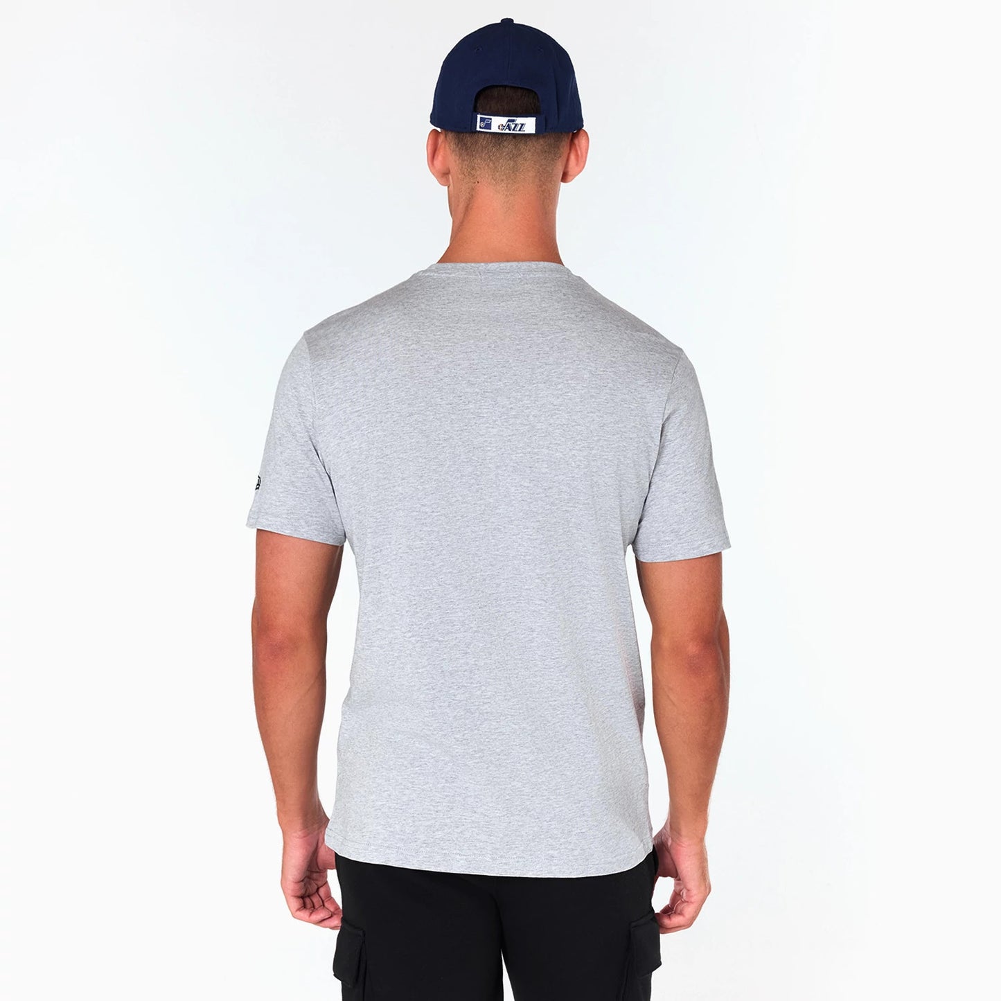 New Era Utah Jazz NBA Grey T-Shirt, rear view showing the plain grey fabric with short sleeves, worn by a model also wearing a navy cap with an embroidered logo on the back, set against a white background.