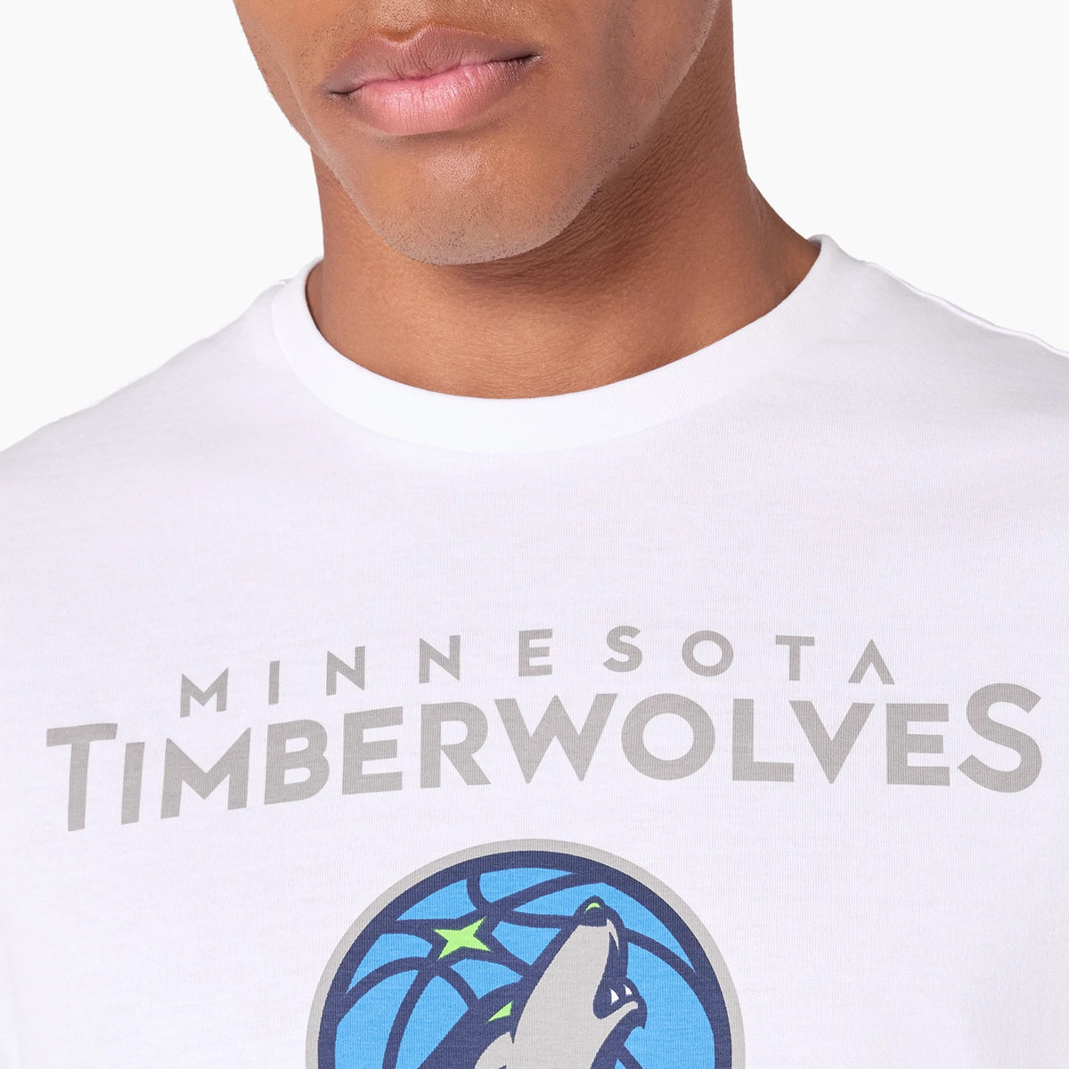 New Era Minnesota Timberwolves NBA White T-Shirt, front view showing a close-up of the chest area with bold grey text of the team name and a colourful logo of a wolf howling at a basketball, on a white background.