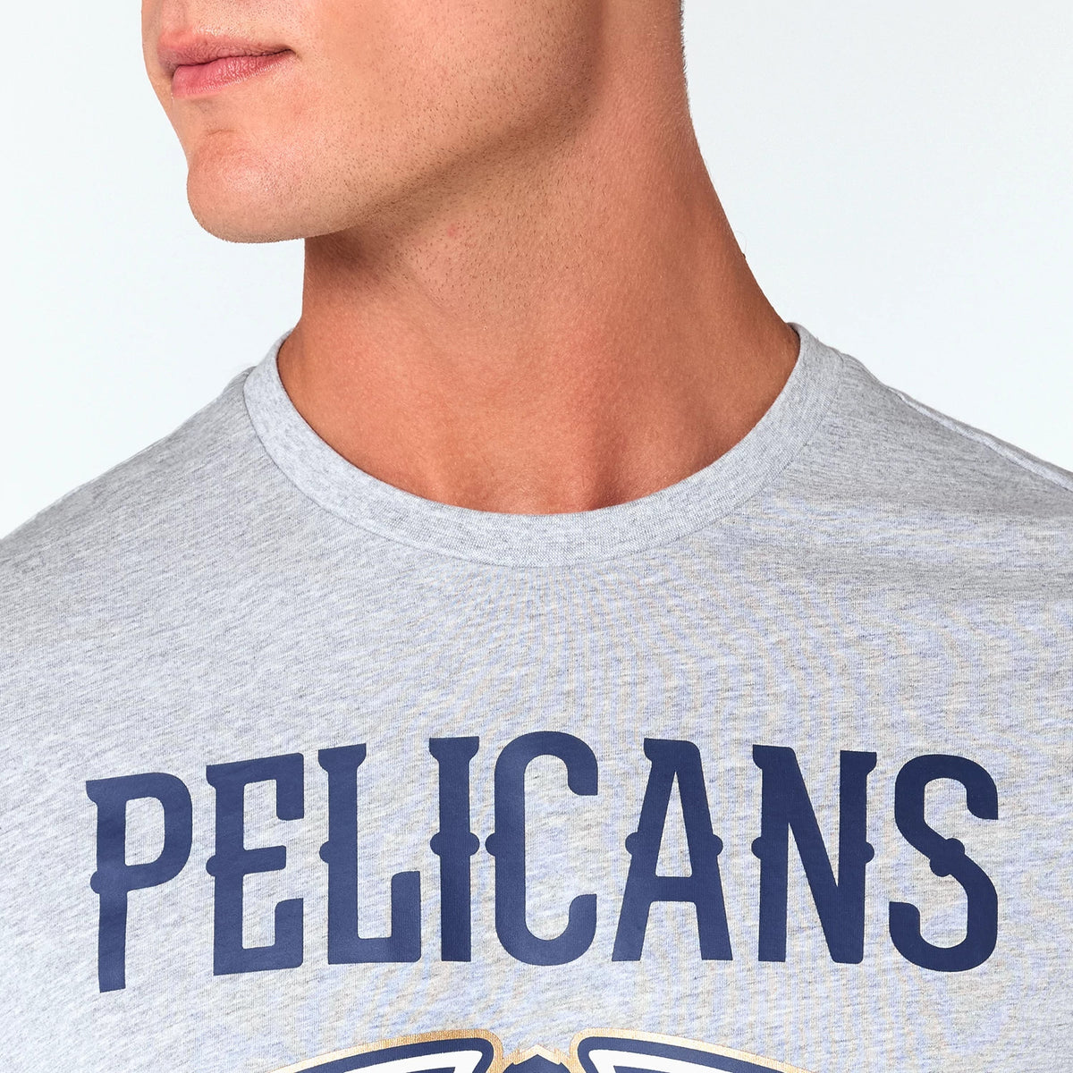 New Era New Orleans Pelicans NBA Grey T-Shirt, front view showing a close-up of the chest with Pelicans printed in large navy blue letters on the light grey fabric with part of the team logo visible below the text.
