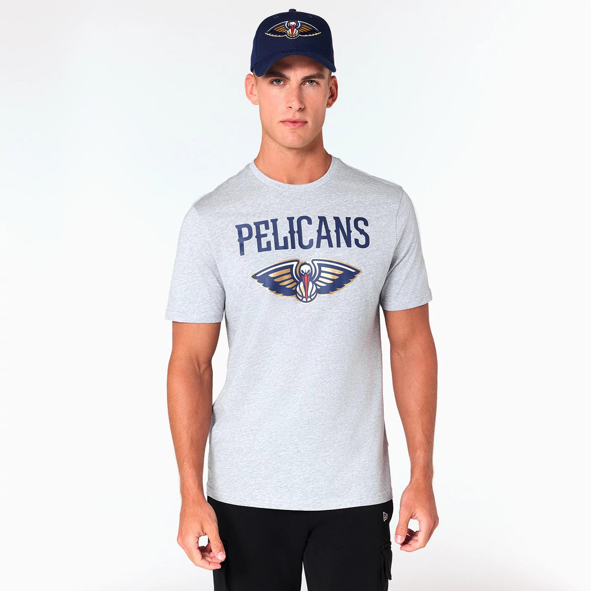 New Era New Orleans Pelicans NBA Grey T-Shirt, on-model view showing the grey tee with the Pelicans logo in colour and 'PELICANS' text across the chest, worn by a model also wearing a navy cap with a raised Pelicans logo.
