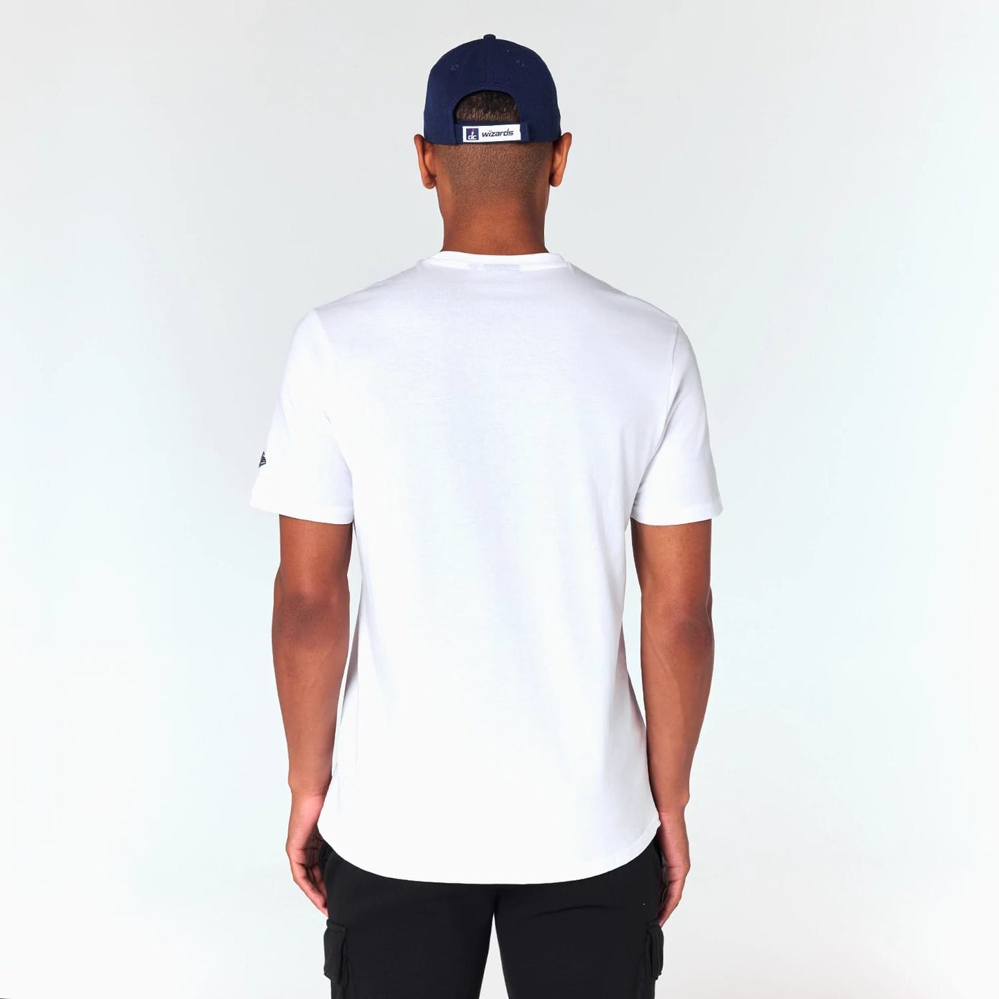 New Era Washington Wizards NBA White T-Shirt, on-model rear view showing a plain white back with the sleeves extending just above the elbows, a small raised logo on the left sleeve, and a blue cap with a Wizards logo at the centre back.