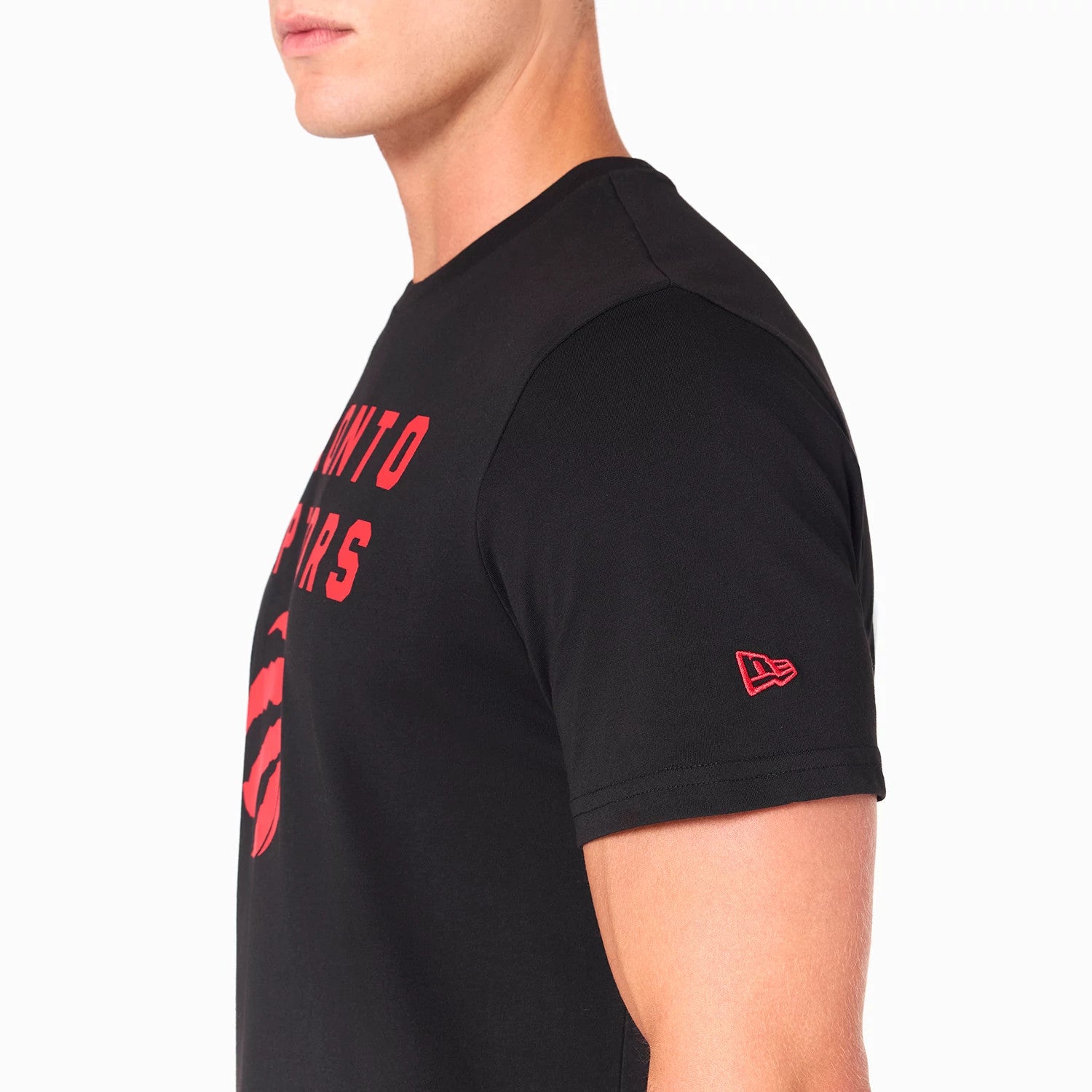 New Era Toronto Raptors NBA Black T-Shirt, side view showing a close-up of the sleeve with a red raised New Era logo, the chest featuring a red Toronto Raptors text and basketball claw graphic on black fabric.