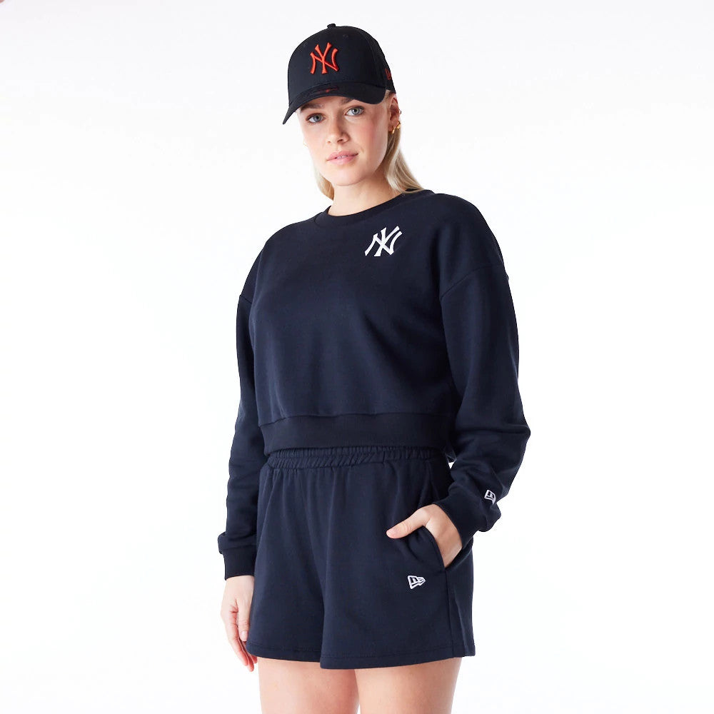 New Era New York Yankees Womens MLB League Essential Black Crop Crew Neck Sweatshirt, front view on a model styled with black shorts and matching cap, featuring a white embroidered NY logo on the left chest.