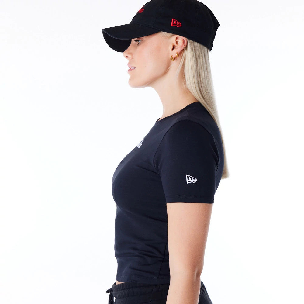 New Era Womens Black Slim T-Shirt, on-model side view showing a black shirt with a raised logo on the sleeve, worn by a person in a black cap with a red debossed logo on the side above the ear.