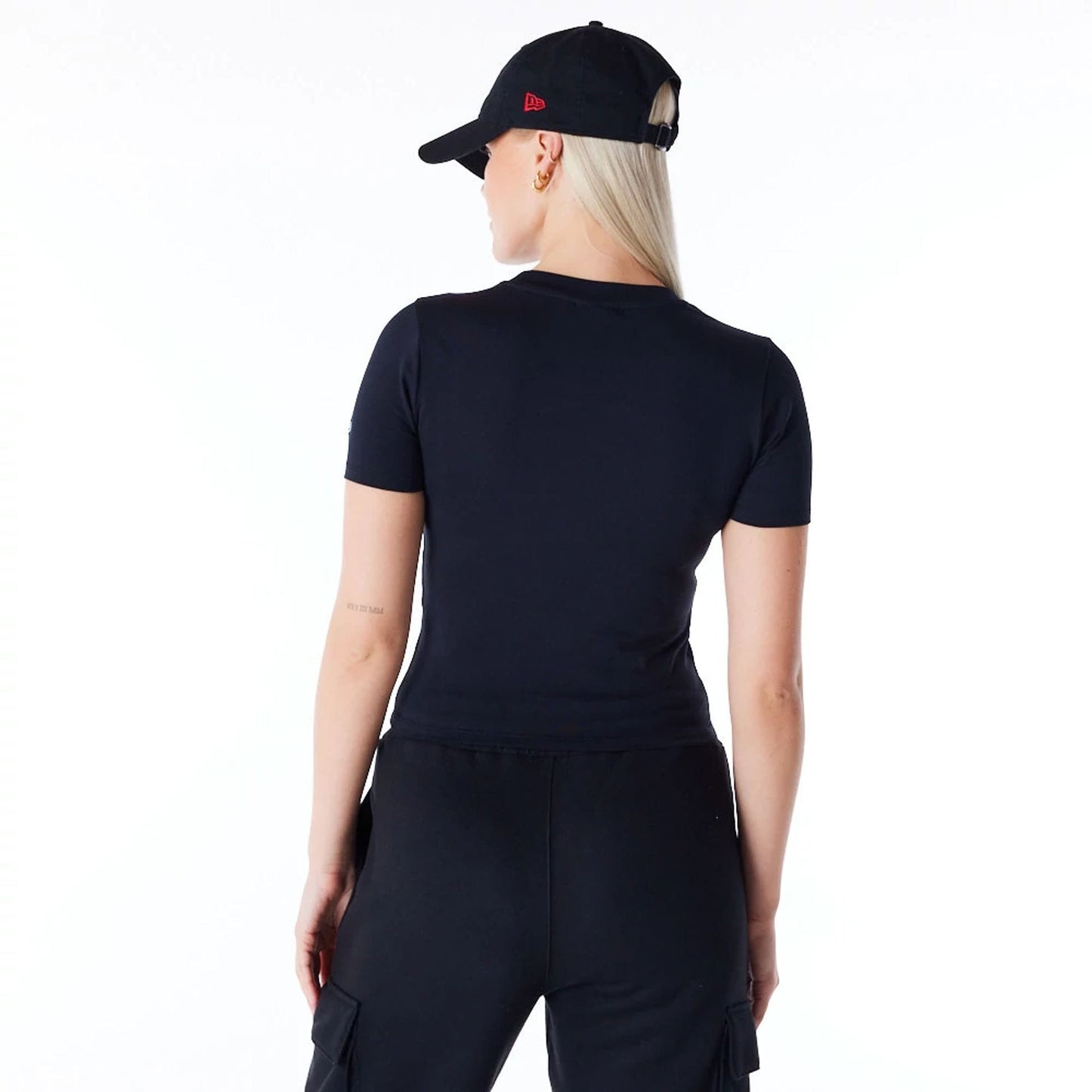 New Era Womens Black Slim T-Shirt, on-model view showing the back of the slim black t-shirt with short sleeves, model wearing a black cap with a red embroidered New Era logo on the side.
