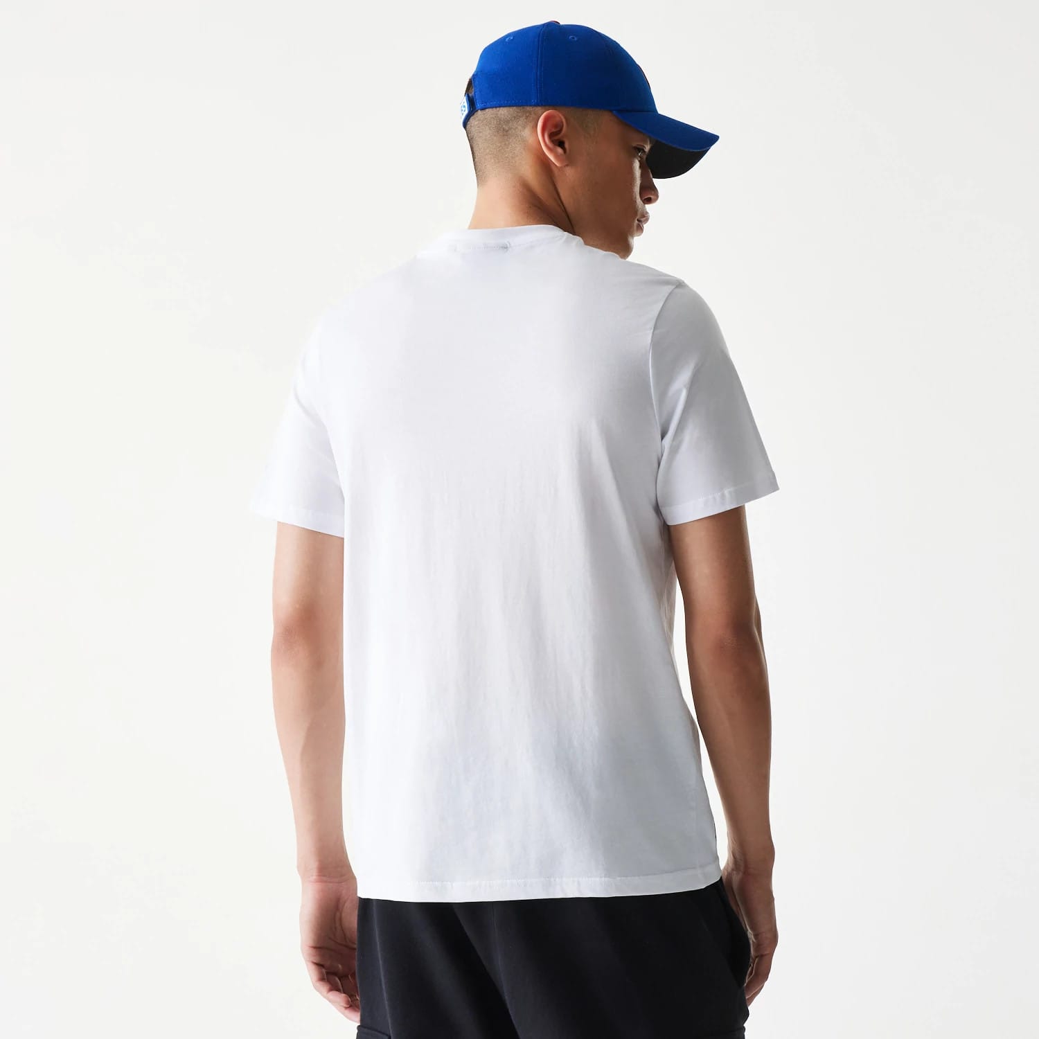 New Era Chicago Cubs MLB Regular White T-Shirt, rear view showing a plain white back with short sleeves, worn by a person in black trousers and a blue cap featuring a raised logo on the back.