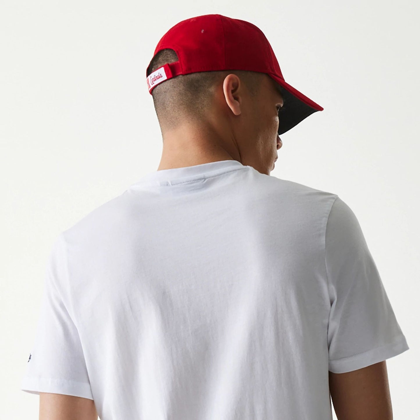 New Era St. Louis Cardinals MLB Regular White T-Shirt, on-model view showing the plain white back of the T-shirt, a red cap worn by the model featuring a debossed Cardinals logo on the rear adjustment strap.
