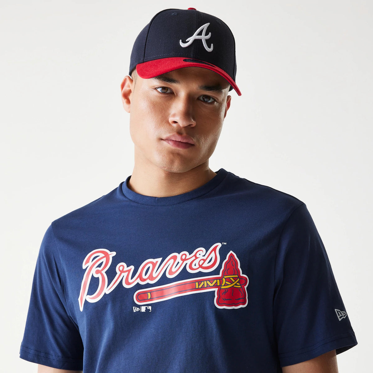 New Era Atlanta Braves MLB Regular Dark Blue T-Shirt, on-model view showing the large red and white Braves script with a tomahawk graphic across the chest, paired with a dark blue cap featuring a raised white A on the front panels.