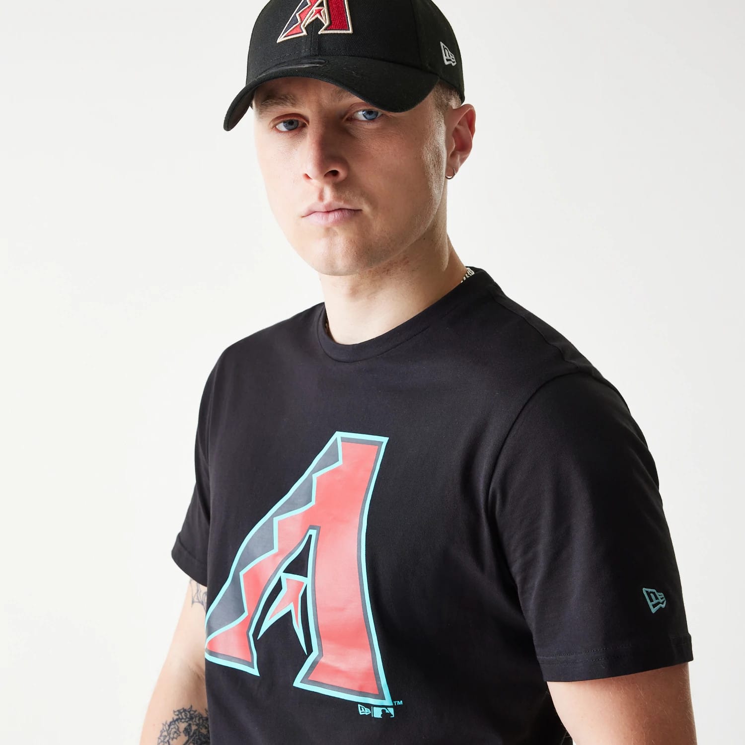 New Era Arizona Diamondbacks MLB Regular Black T-Shirt, on-model view showing a large stylised red and turquoise 'A' logo across the chest, paired with a black cap featuring a raised team logo on the front and an embroidered New Era logo on the side.