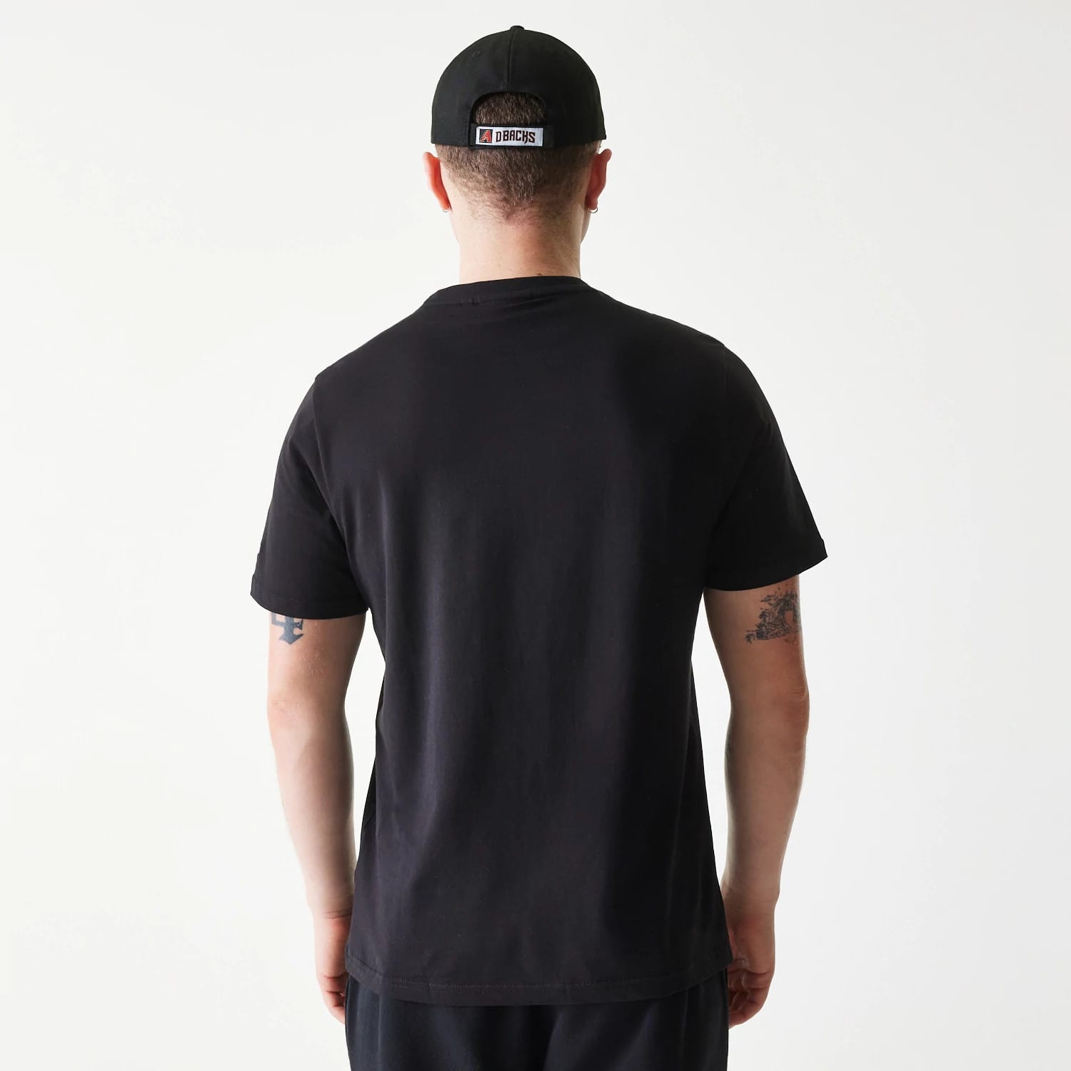 New Era Arizona Diamondbacks MLB Regular Black T-Shirt, on-model rear view showing the plain black back of the T-shirt, a man wearing a black cap with an Arizona Diamondbacks logo embroidered on the back, and tattoos on his arms.
