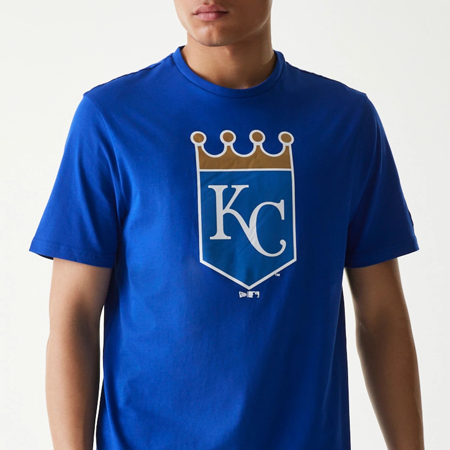 New Era Kansas City Royals MLB Regular Blue T-Shirt, front view showing a blue round-neck T-shirt with a large white and gold crowned KC logo on the chest, worn by a model from the waist up.