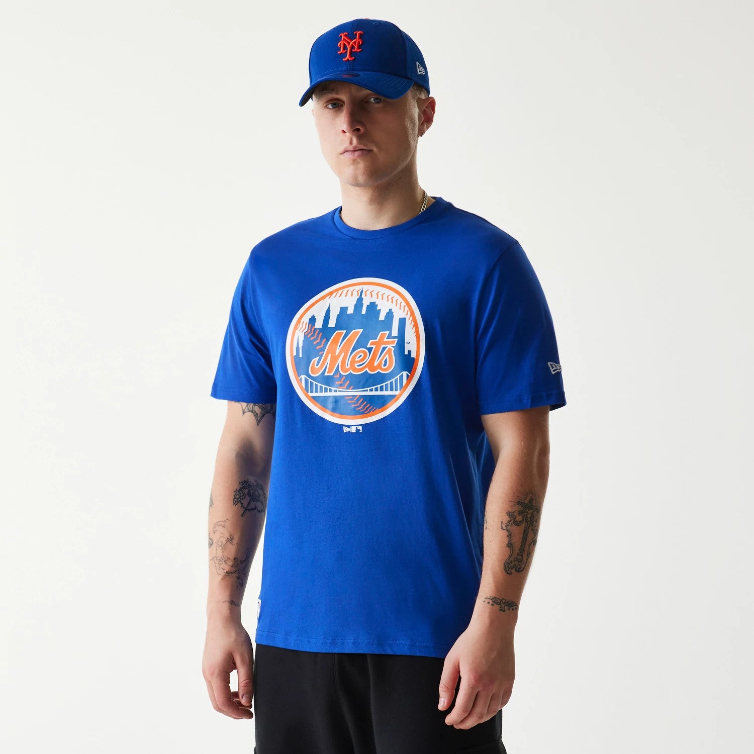 New Era New York Mets MLB Regular Blue T-Shirt, on-model view showing a blue crew-neck shirt with the Mets logo in orange and white on the chest, model also wearing a matching blue cap with an embroidered Mets logo in orange.