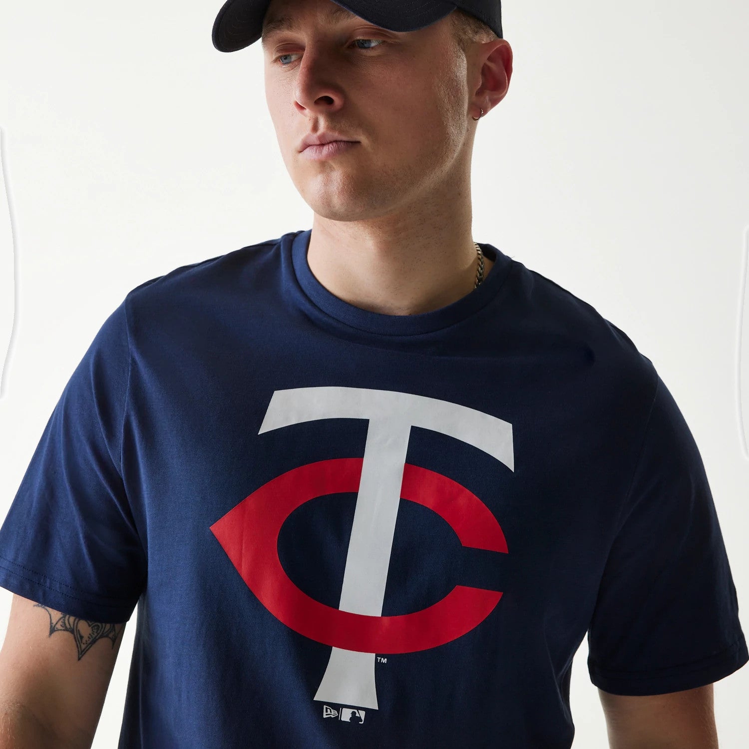New Era Minnesota Twins MLB Regular Dark Blue T-Shirt, on-model view showing a large white and red logo centred on the chest, worn by a person in a black cap with a debossed New Era logo on the front of the cap.