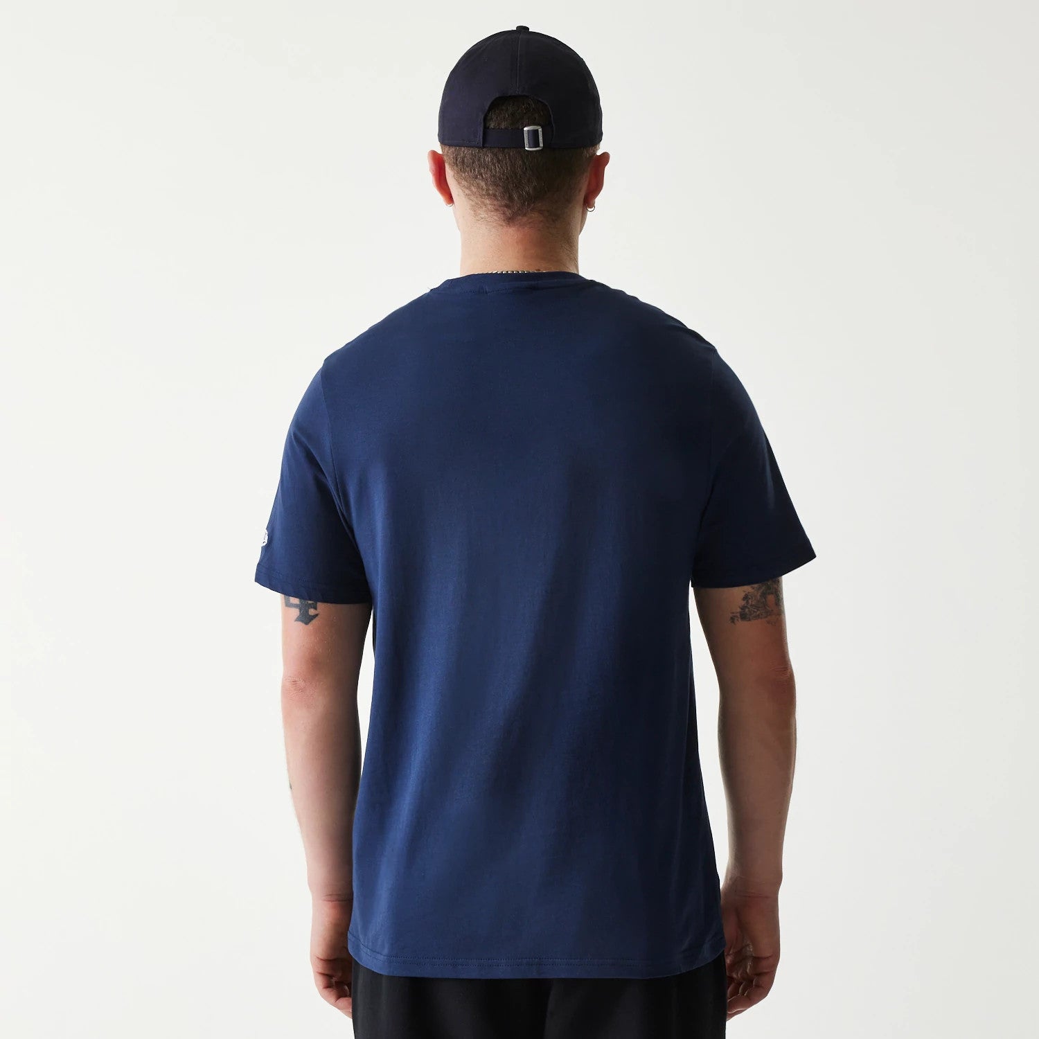 New Era Minnesota Twins MLB Regular Dark Blue T-Shirt, on-model view showing the plain dark blue back of the t-shirt with short sleeves, worn by a man with tattoos and a dark blue cap featuring a debossed logo on the rear.