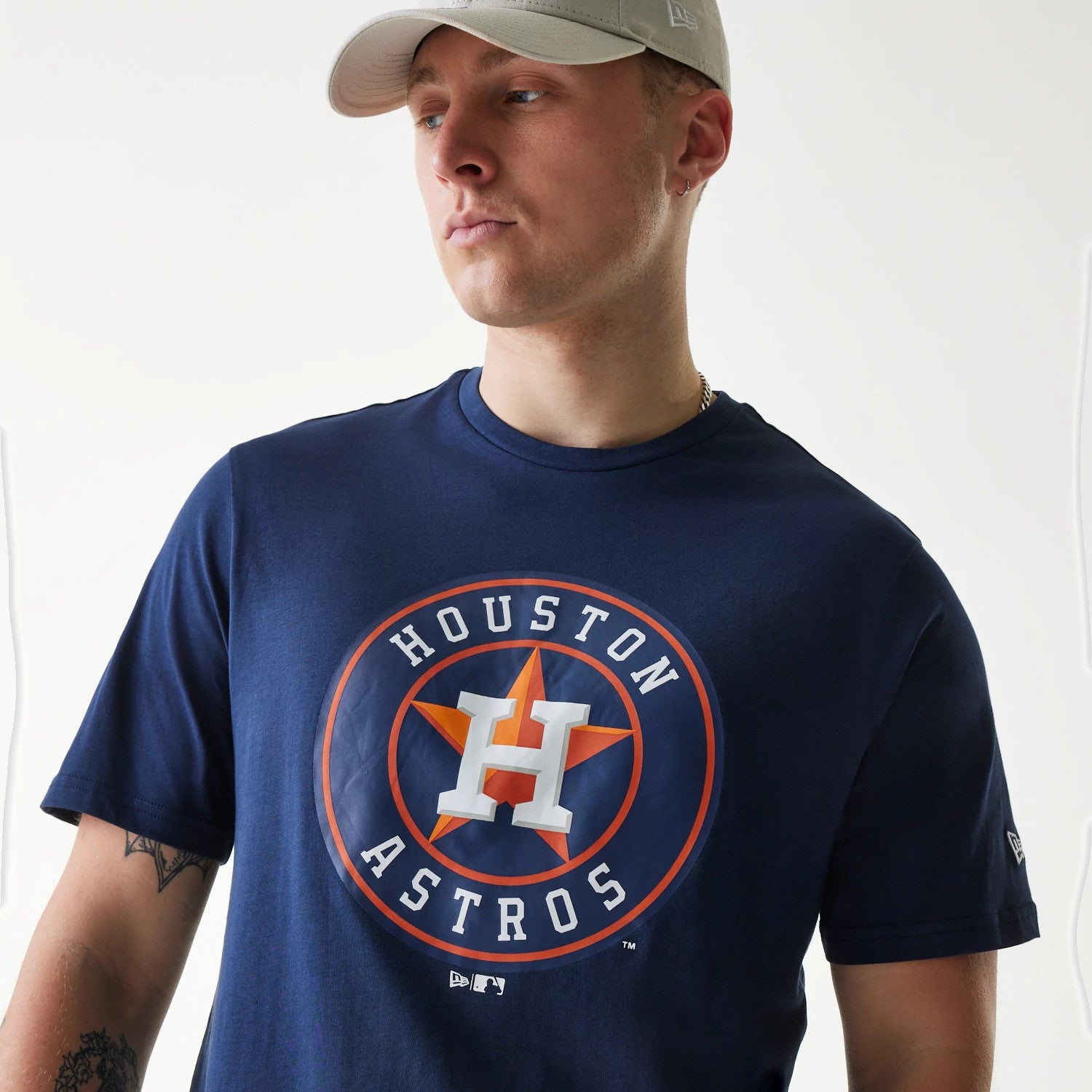 New Era Houston Astros MLB Regular Dark Blue T-Shirt, front view showing a large Houston Astros logo printed in orange and white on the chest, worn by a person with a light beige cap featuring a raised New Era logo on the side.