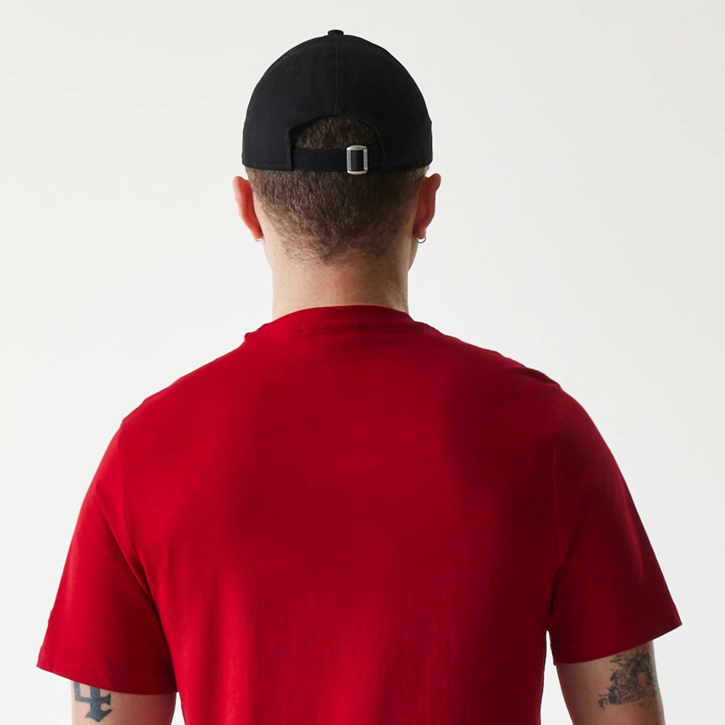 New Era Cincinnati Reds MLB Regular Red T-Shirt, on-model view showing the back of a person wearing the red T-shirt, paired with a black cap having a buckle closure and a row of eyelets around the crown.