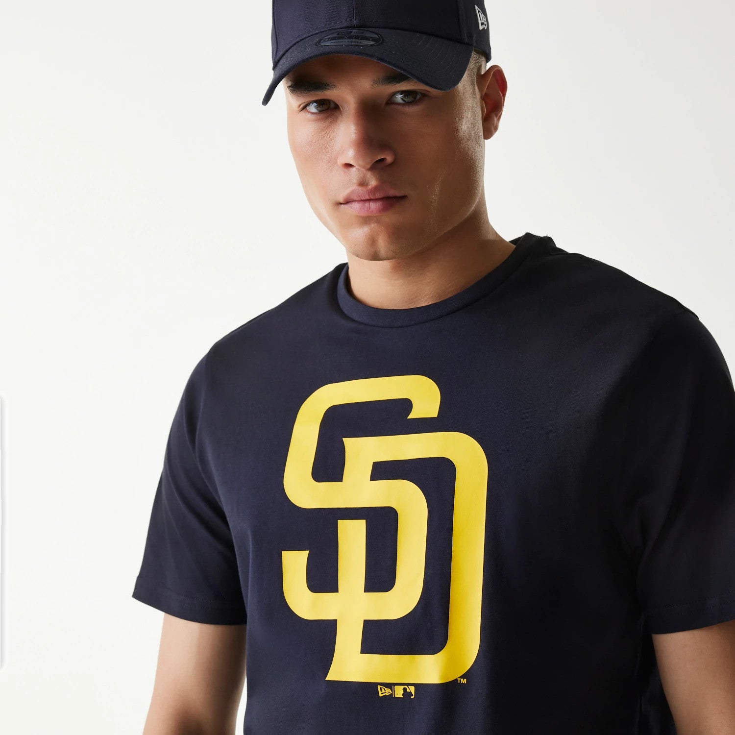 New Era San Diego Padres MLB Regular Navy T-Shirt, front view showing the large yellow SD logo printed on the chest, a man wearing the navy shirt paired with a navy cap featuring a debossed New Era logo on the side.
