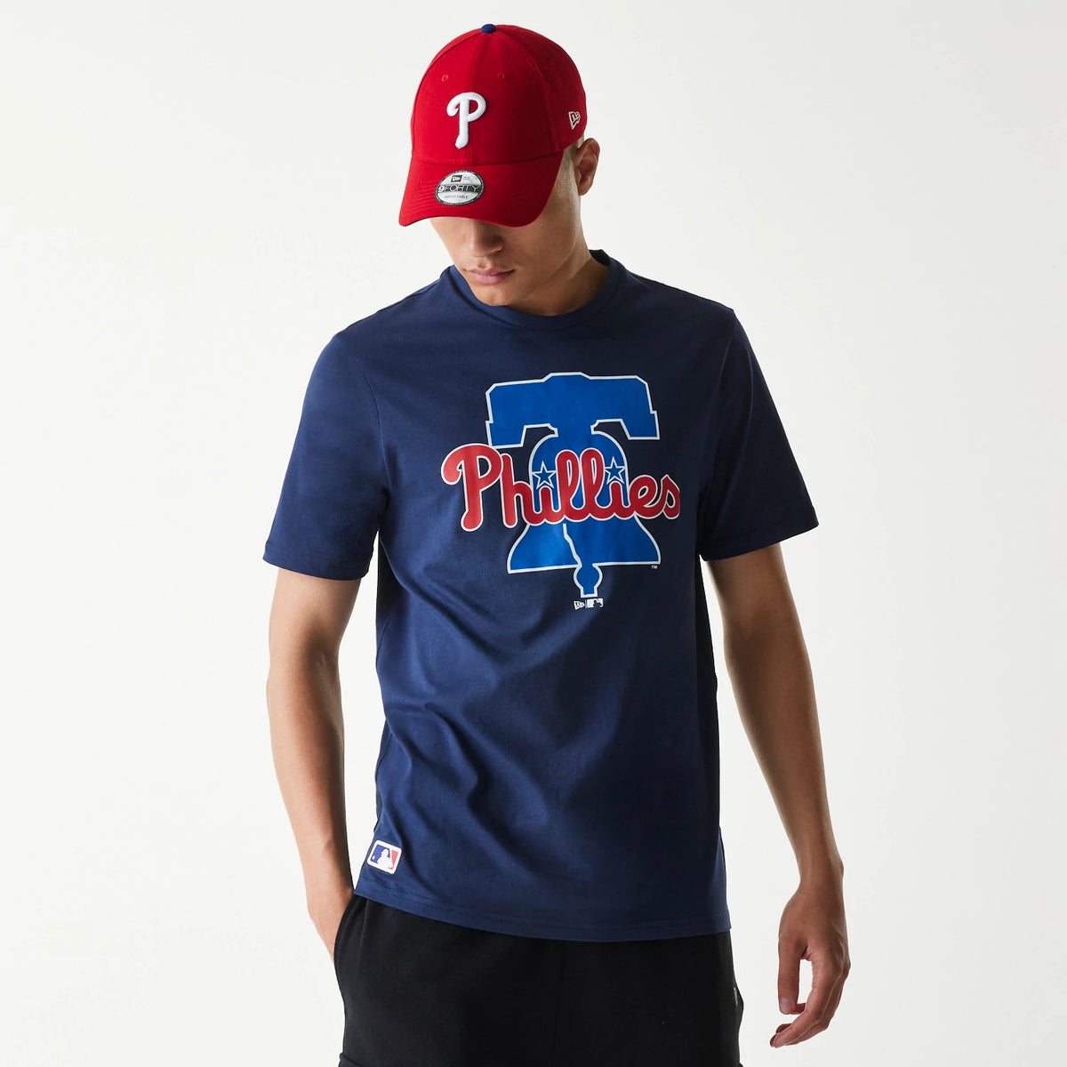 New Era Philadelphia Phillies MLB Regular Dark Blue T-Shirt, on-model view showing a large red and white Phillies graphic on the chest against a dark blue background, worn with a red cap featuring a raised white P on the front.