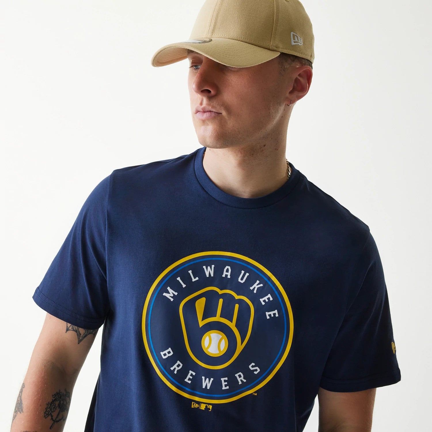 New Era Milwaukee Brewers MLB Regular Dark Blue T-Shirt, on-model view showing a large printed logo of the Milwaukee Brewers on the chest, paired with a beige cap featuring a raised New Era logo on the side.