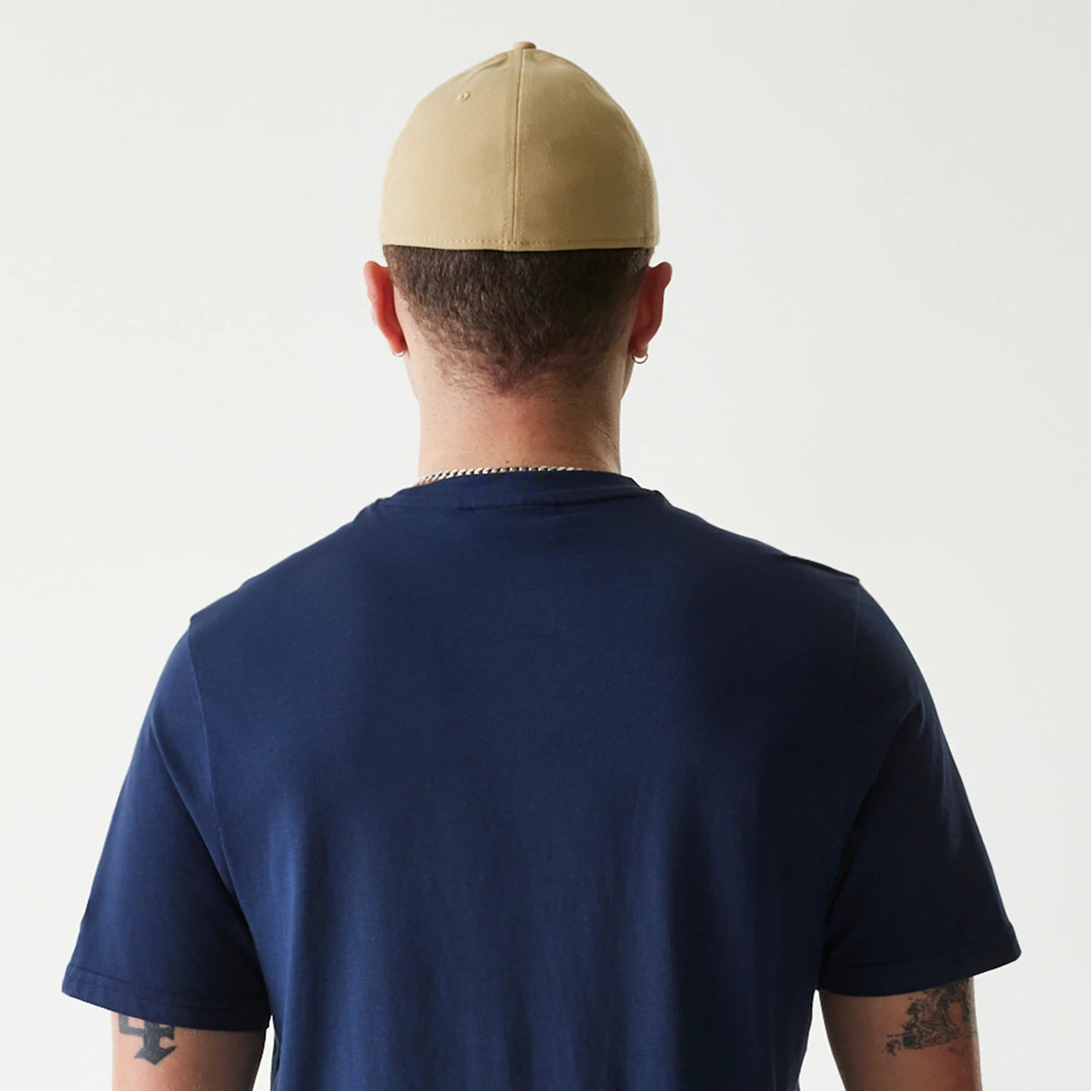 New Era Milwaukee Brewers MLB Regular Dark Blue T-Shirt, rear view showing the plain dark blue fabric with short sleeves, worn on-model with a beige cap, highlighting the simple design from the back.