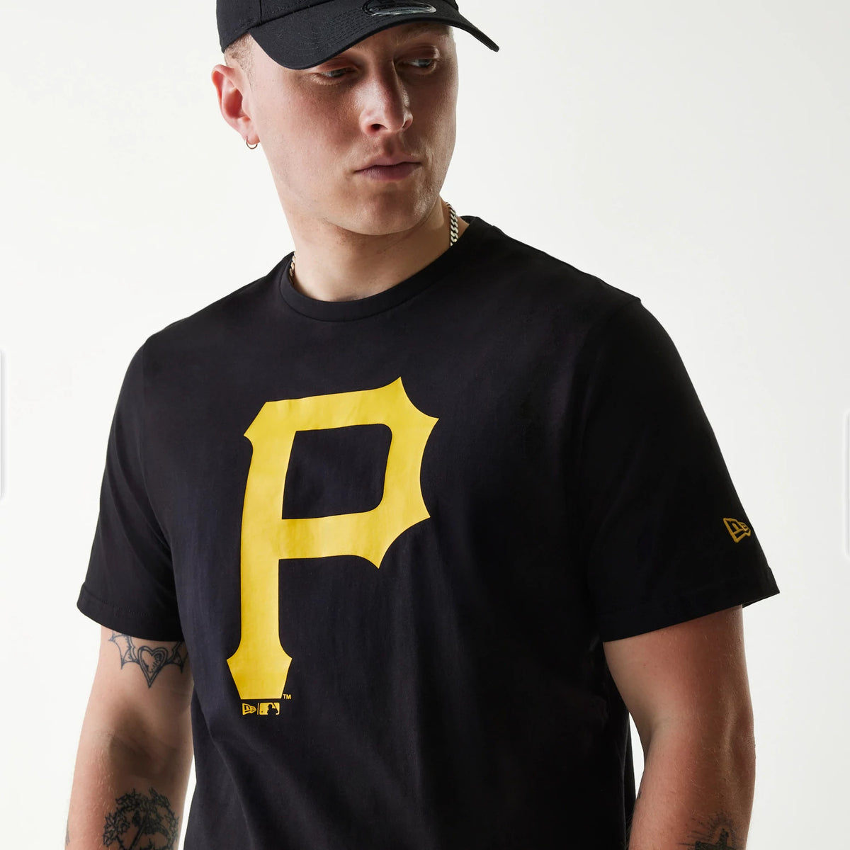 New Era Pittsburgh Pirates MLB Regular Black T-Shirt, on-model view showing a large yellow P printed on the chest, the wearer with a black cap, and a small yellow debossed New Era logo on the left sleeve.