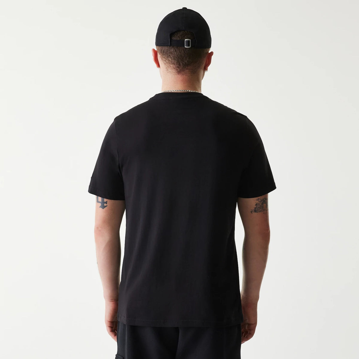 New Era Pittsburgh Pirates MLB Regular Black T-Shirt, on-model back view showing the plain black fabric extending to short sleeves, worn with a black cap featuring a debossed logo and adjustable strap at the back.
