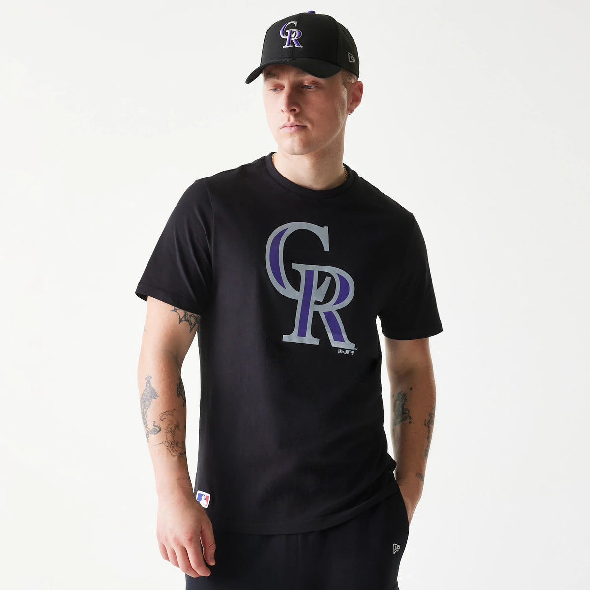New Era Colorado Rockies MLB Regular Black T-Shirt, on-model view showing the large purple and grey CR logo centred on the chest, a small tag on the lower side and the New Era logo on a black cap worn by the model.
