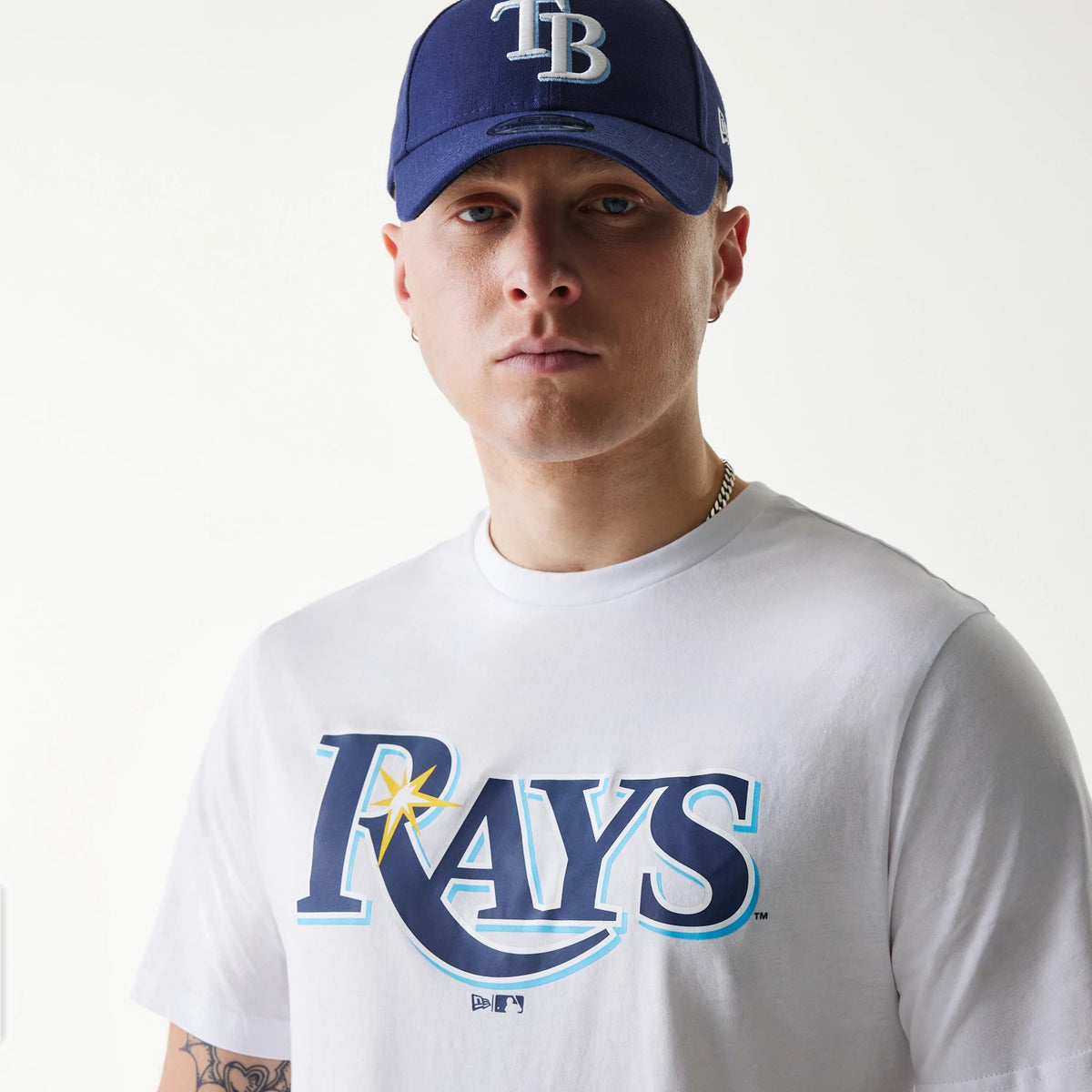 New Era Tampa Bay Rays MLB Regular White T-Shirt, on-model view showing a large blue and yellow Rays logo printed across the chest, paired with a blue cap featuring a raised white TB logo on the front.