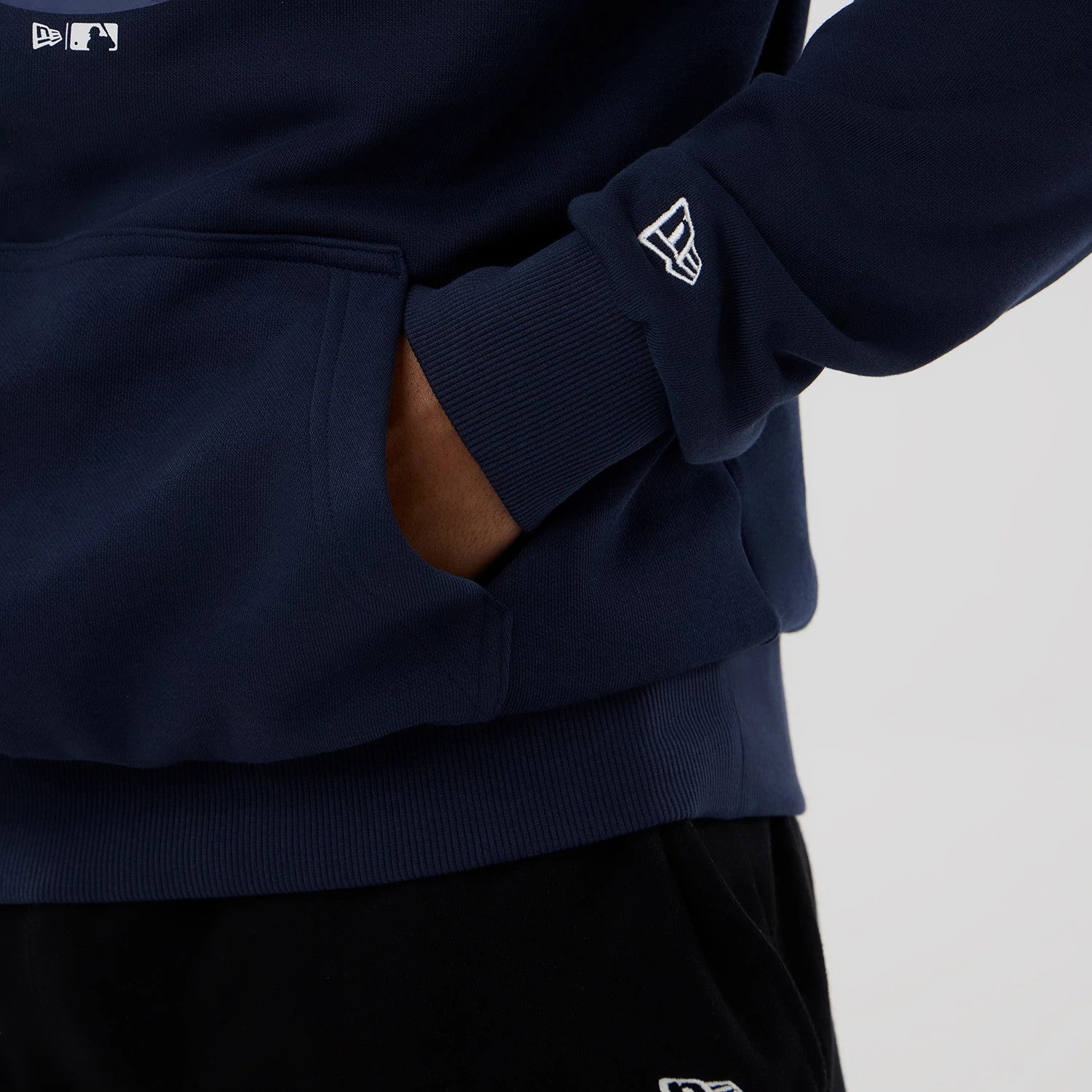 New Era Houston Astros MLB Dark Blue Pullover Hoodie, side view showing a close-up of the dark blue fabric with a ribbed hem, a raised New Era logo on the sleeve cuff, and a front pocket with a hand partially inside.