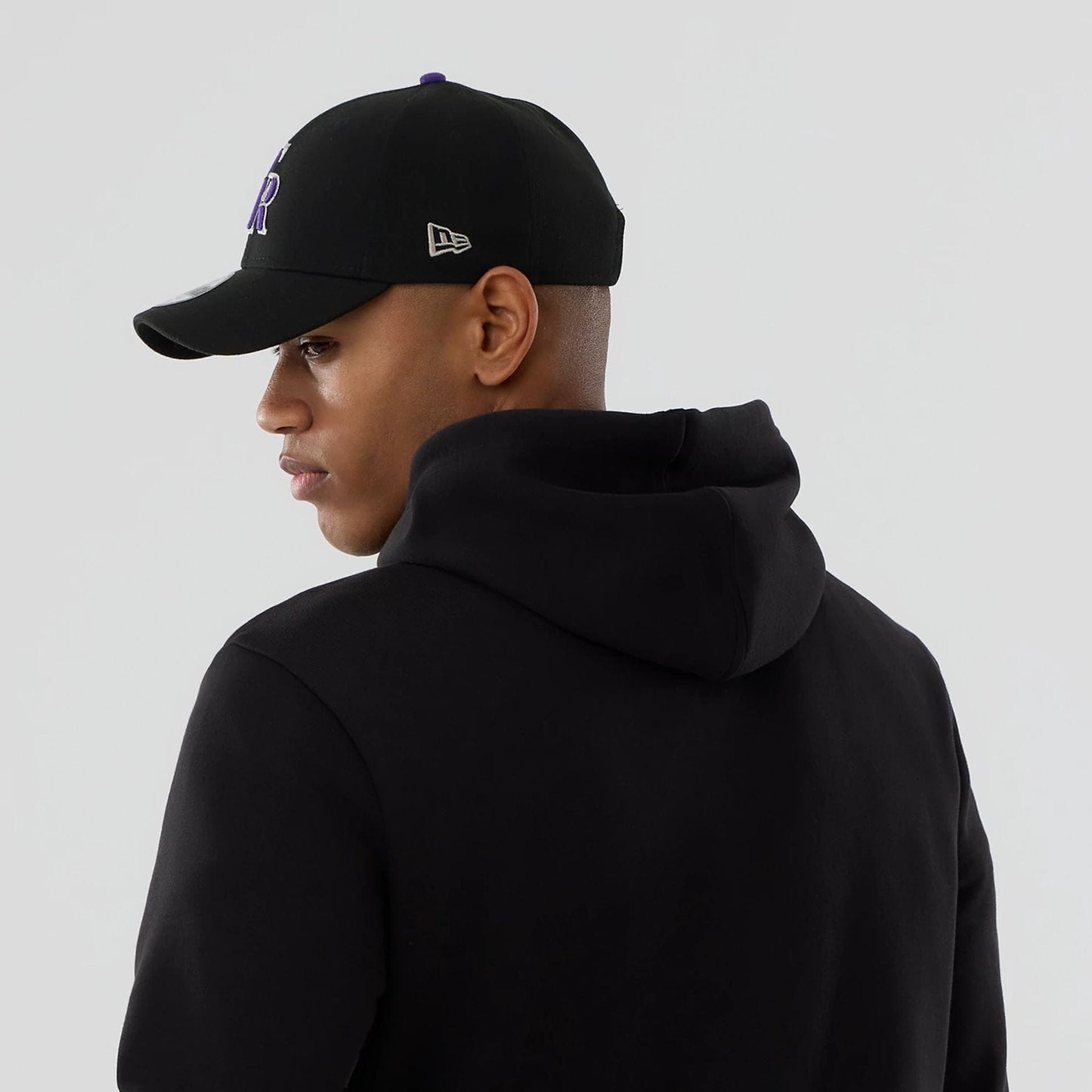 New Era Colorado Rockies MLB Black Pullover Hoodie, on-model view showing the back of the black hoodie with a hood resting on the shoulders, a black cap with a raised CR logo on the front and a debossed New Era logo on the side.