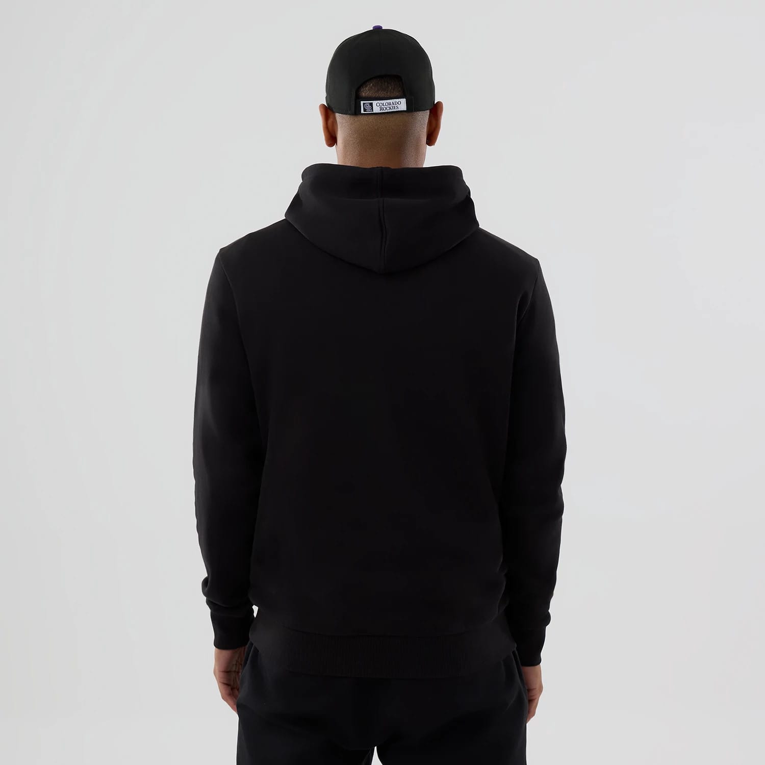 New Era Colorado Rockies MLB Black Pullover Hoodie, rear view showing a plain black hoodie with a relaxed fit, the hood resting on the back, on-model wearing a black cap with a label.
