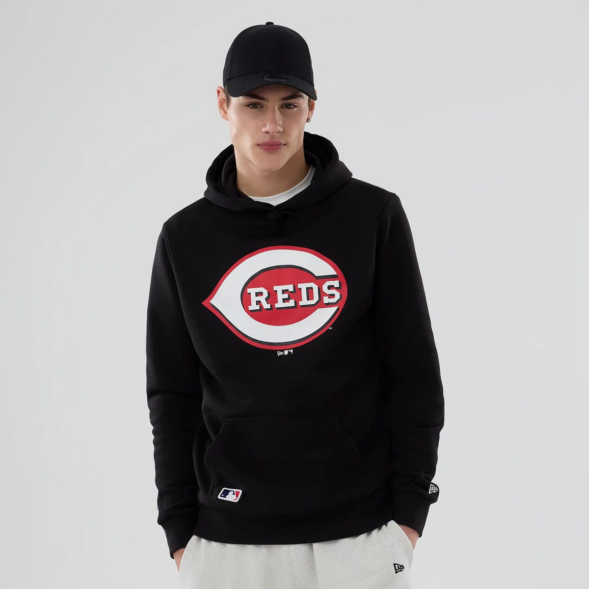 New Era Cincinnati Reds MLB Black Pullover Hoodie, on-model view showing a large red and white logo on the front centre, a kangaroo pocket below, New Era flag on the left sleeve, and a black cap with a debossed logo.