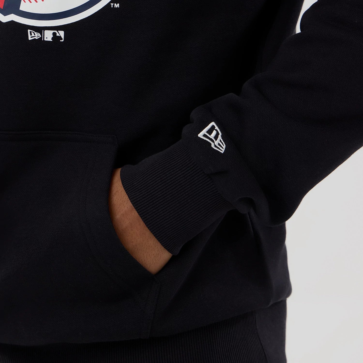 New Era Cleveland Guardians MLB Navy Pullover Hoodie, side view showing the ribbed cuff with an embroidered New Era logo on the sleeve and a person's hand resting in the front kangaroo pocket.