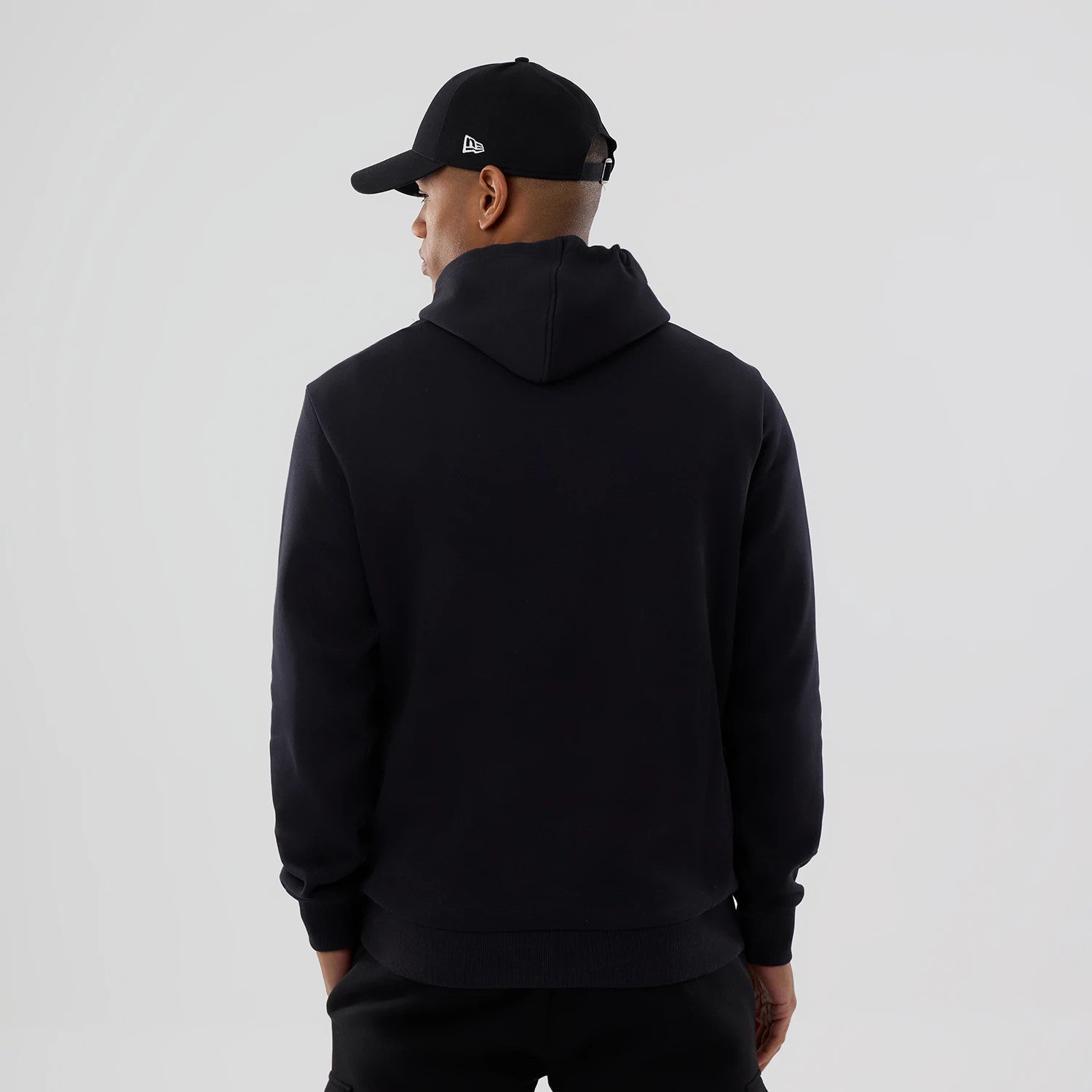 New Era Cleveland Guardians MLB Navy Pullover Hoodie, rear view showing the plain navy back with a relaxed hood and long sleeves, worn by a person also in a black cap with an embossed logo on the side.