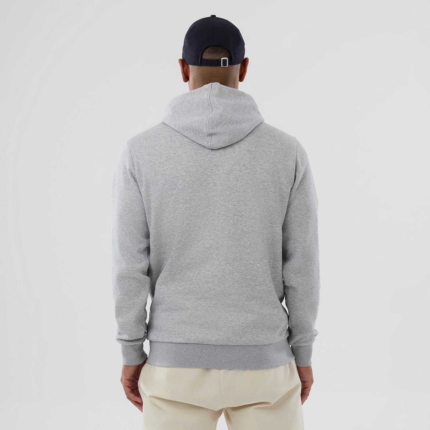 New Era Chicago Cubs MLB Grey Pullover Hoodie, rear view showing the plain grey back with an attached hood, ribbed cuffs and hem, worn by a person in beige trousers and a dark cap with an eyelet and strap at the back.