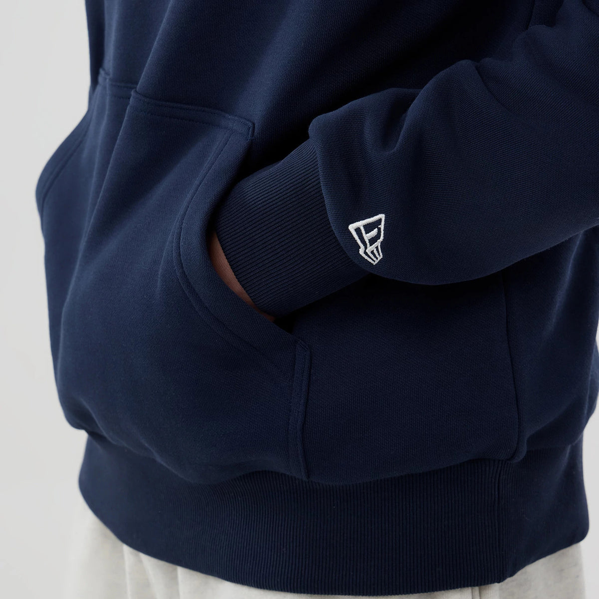 New Era Washington Nationals MLB Dark Blue Pullover Hoodie, side view focusing on the dark blue fabric with a kangaroo pocket, ribbed cuffs, and a white embroidered logo on the sleeve near the wrist.