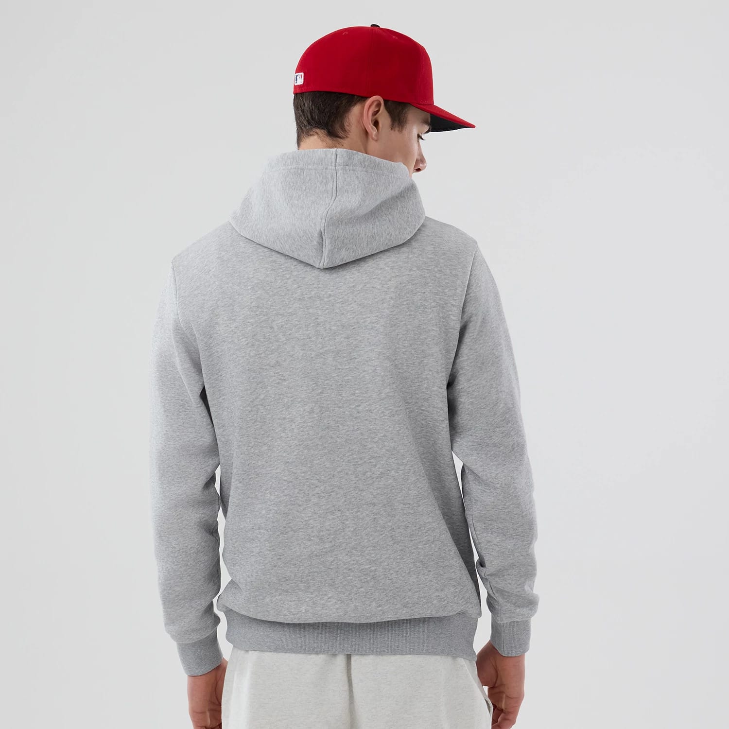 New Era Philadelphia Phillies MLB Grey Pullover Hoodie, rear view showing the simple grey hood and ribbed waistband, worn by a model also wearing a red cap with a white logo on the back.