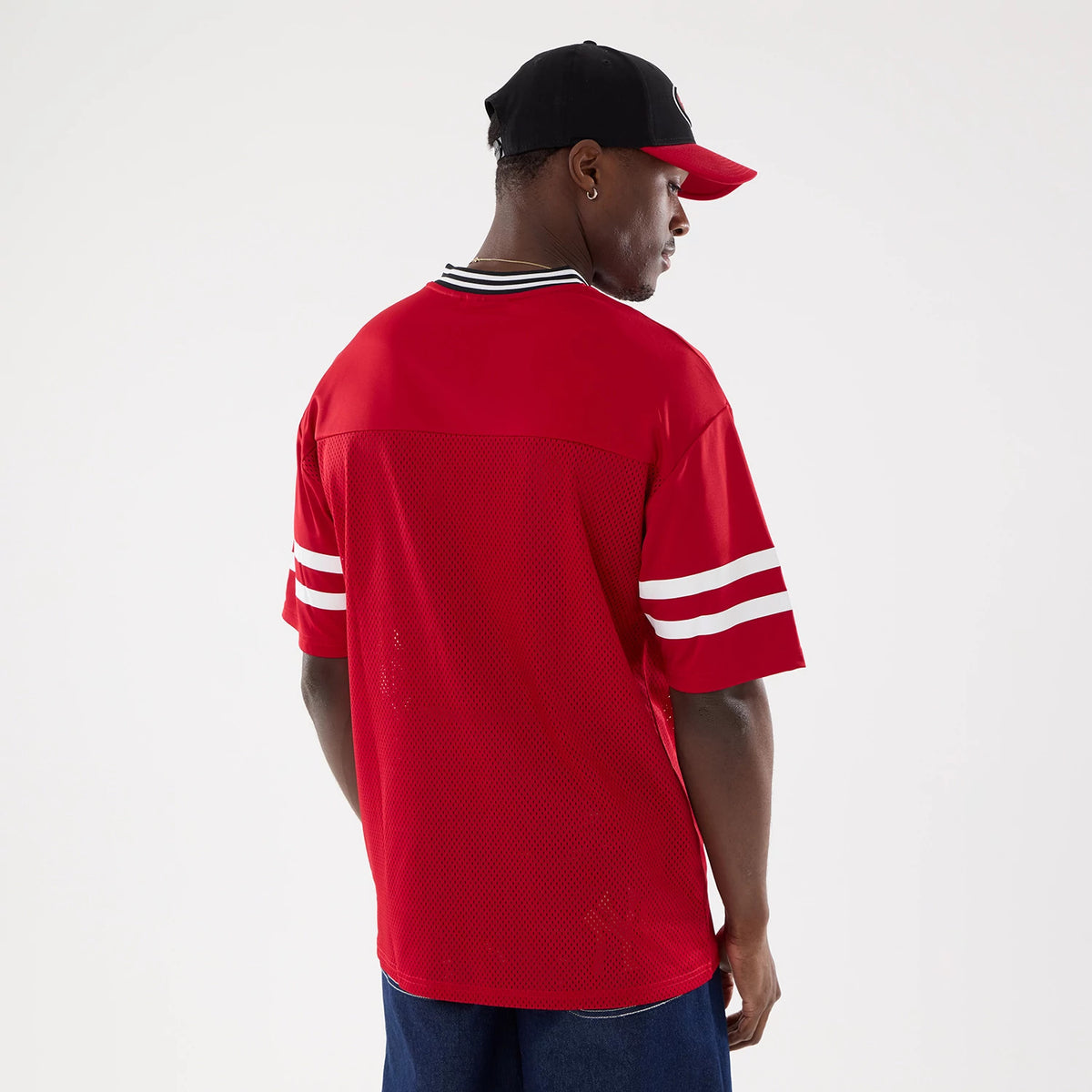 New Era San Francisco 49ers NFL Mesh Red Mesh Jersey, back view on a model wearing a matching cap, featuring double white stripe detailing on the sleeves and a ribbed black and white collar.