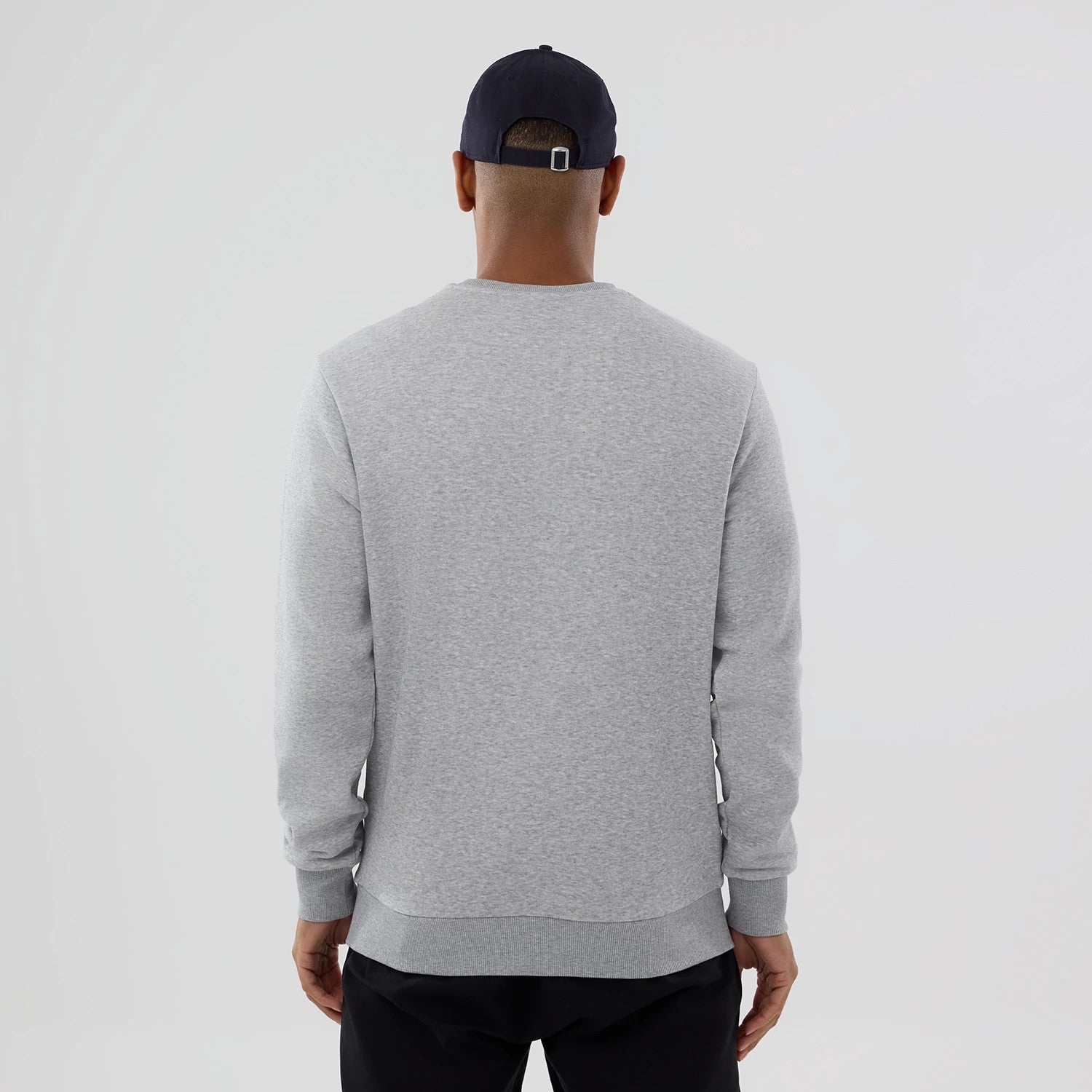 New Era MLB Generic Logo Grey Crew Neck Sweater, back view on a model wearing a dark cap, showing the simple heather grey design with ribbed cuffs and waistband, offering a casual yet clean look.