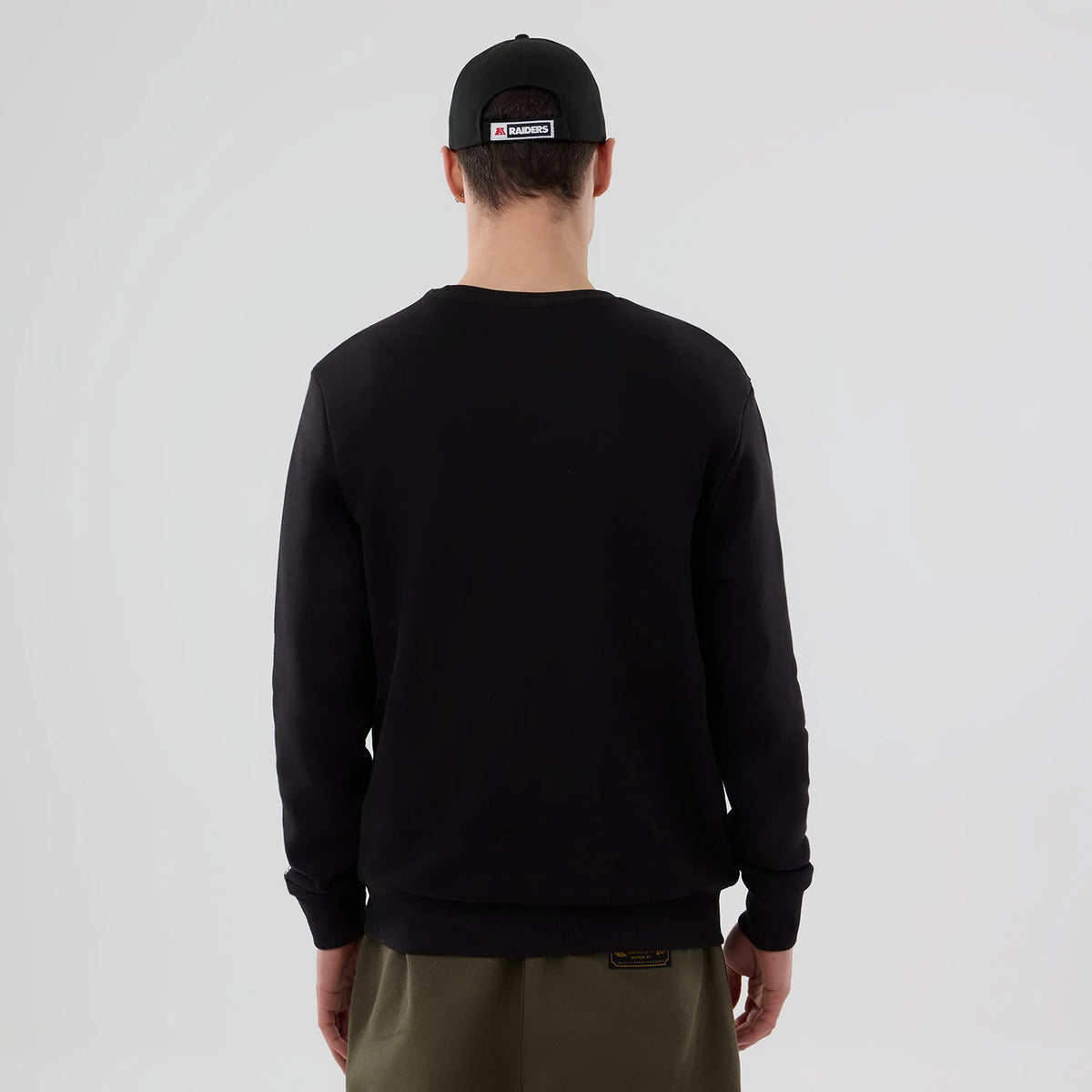 New Era Las Vegas Raiders NFL Core Black Crew Neck Sweater, back view on a model, showing the plain black design paired with a black cap featuring the Raiders logo embroidered on the centre back.