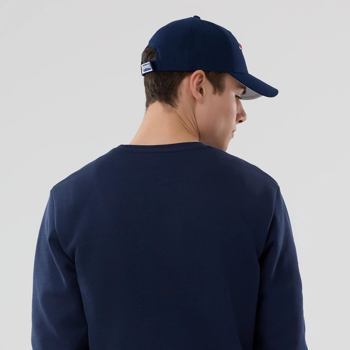 New Era New England Patriots NFL Dark Blue Crew Neck Sweater, rear view on a model with a matching dark blue cap featuring a Patriots logo on the right side and a structured crown.
