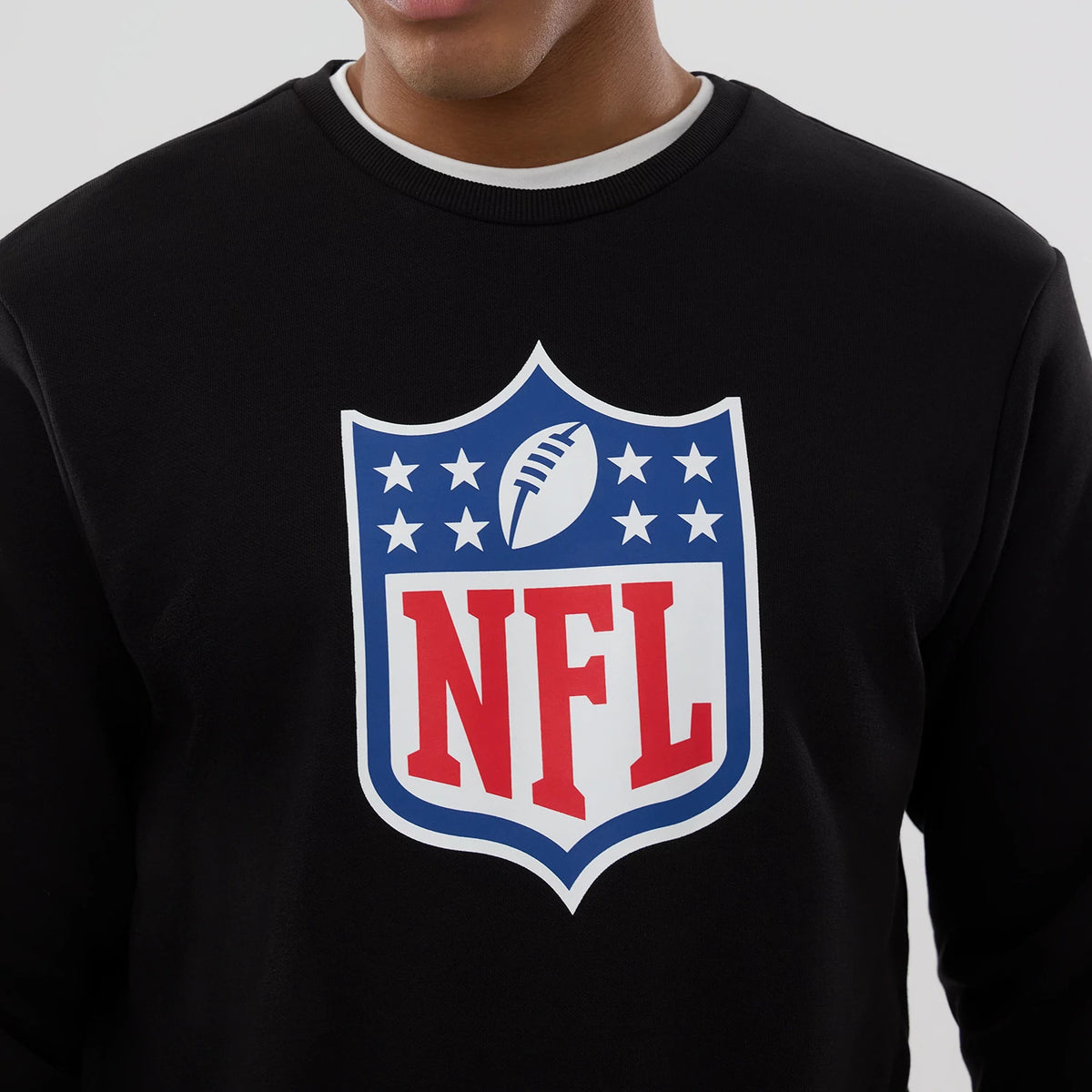 New Era NFL Generic Logo Black Crew Neck Sweater, front view on a model showing the large red, white and blue NFL logo centred on the chest against the black fabric, with a ribbed collar showing a white undershirt.