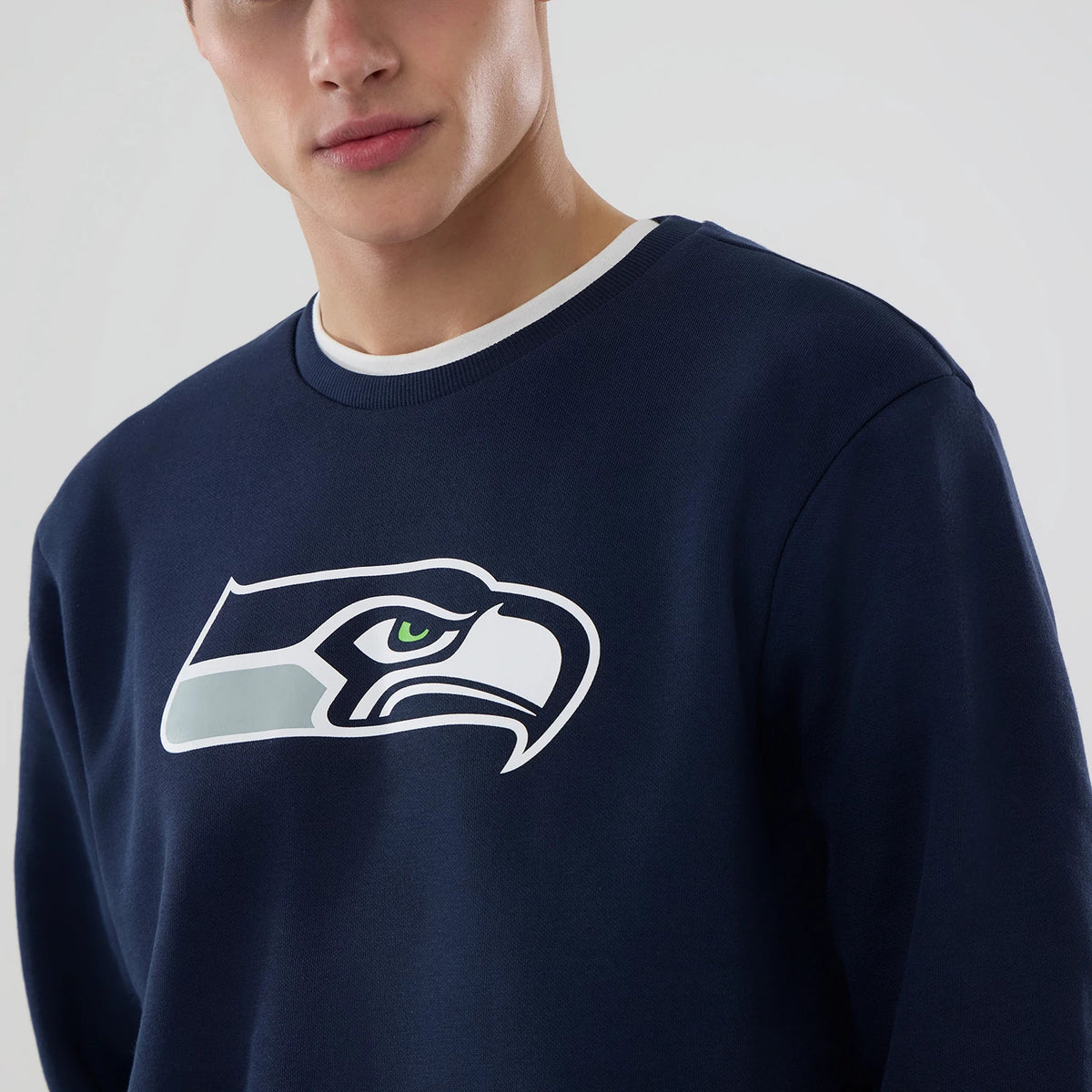 New Era Seattle Seahawks NFL Dark Blue Crew Neck Sweater, front view on a model wearing a white undershirt, featuring the large white and green Seahawks logo prominently printed on the chest.