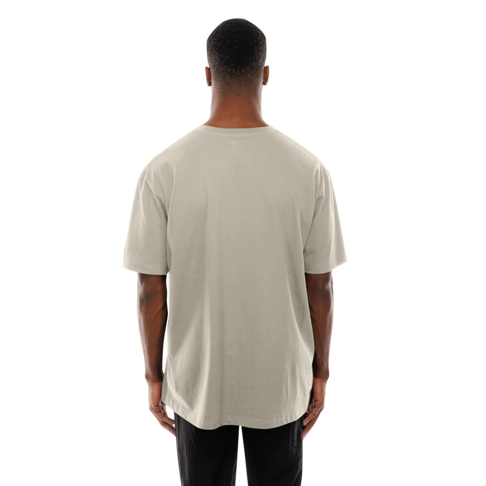 New Era LA Lakers Modern Driver Light Beige T-Shirt, rear view showing the plain light beige back with short sleeves, rounded neckline, and straight hemline draped over black trousers worn by a standing model.