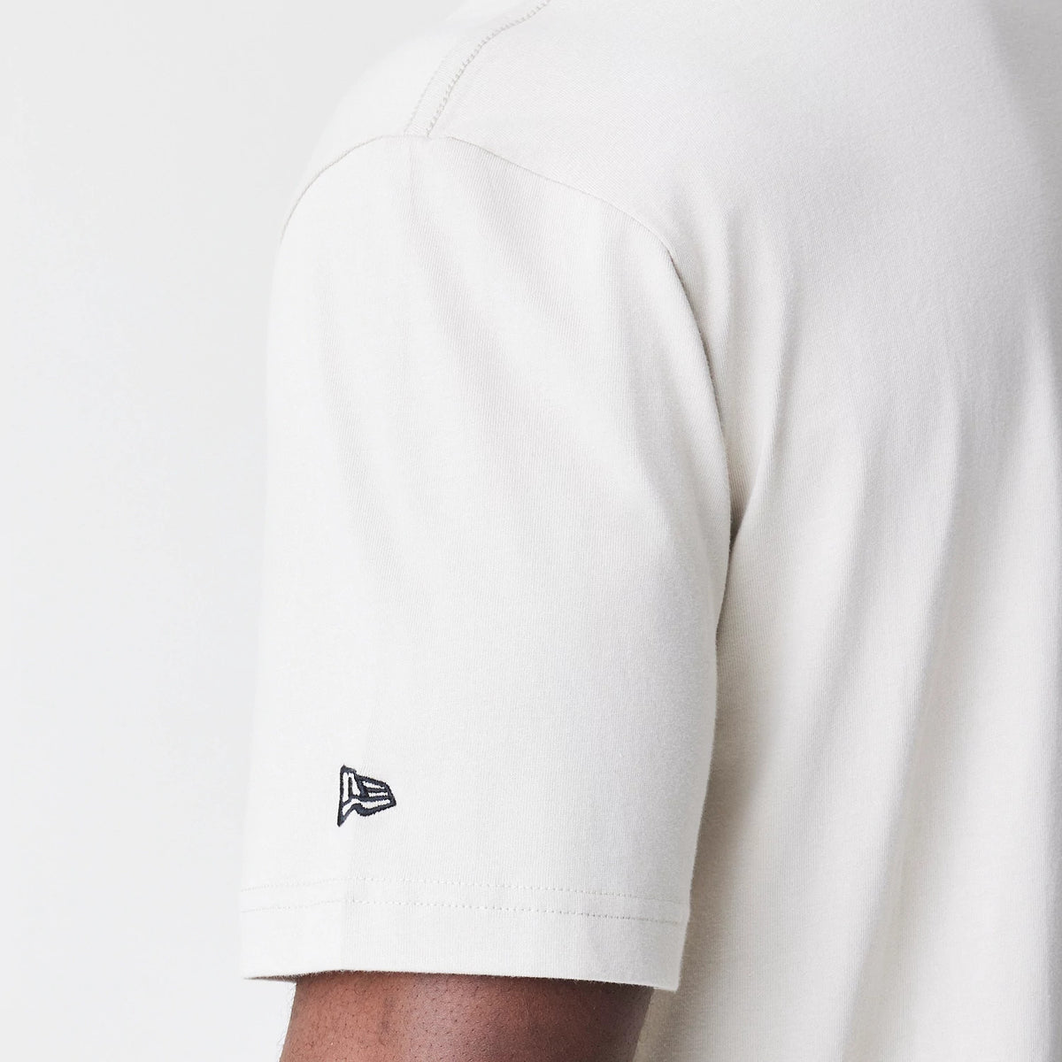 New Era Chicago Bulls Modern Driver Light Beige T-Shirt, side view showing the short sleeve with a raised New Era logo embroidered in black near the cuff.